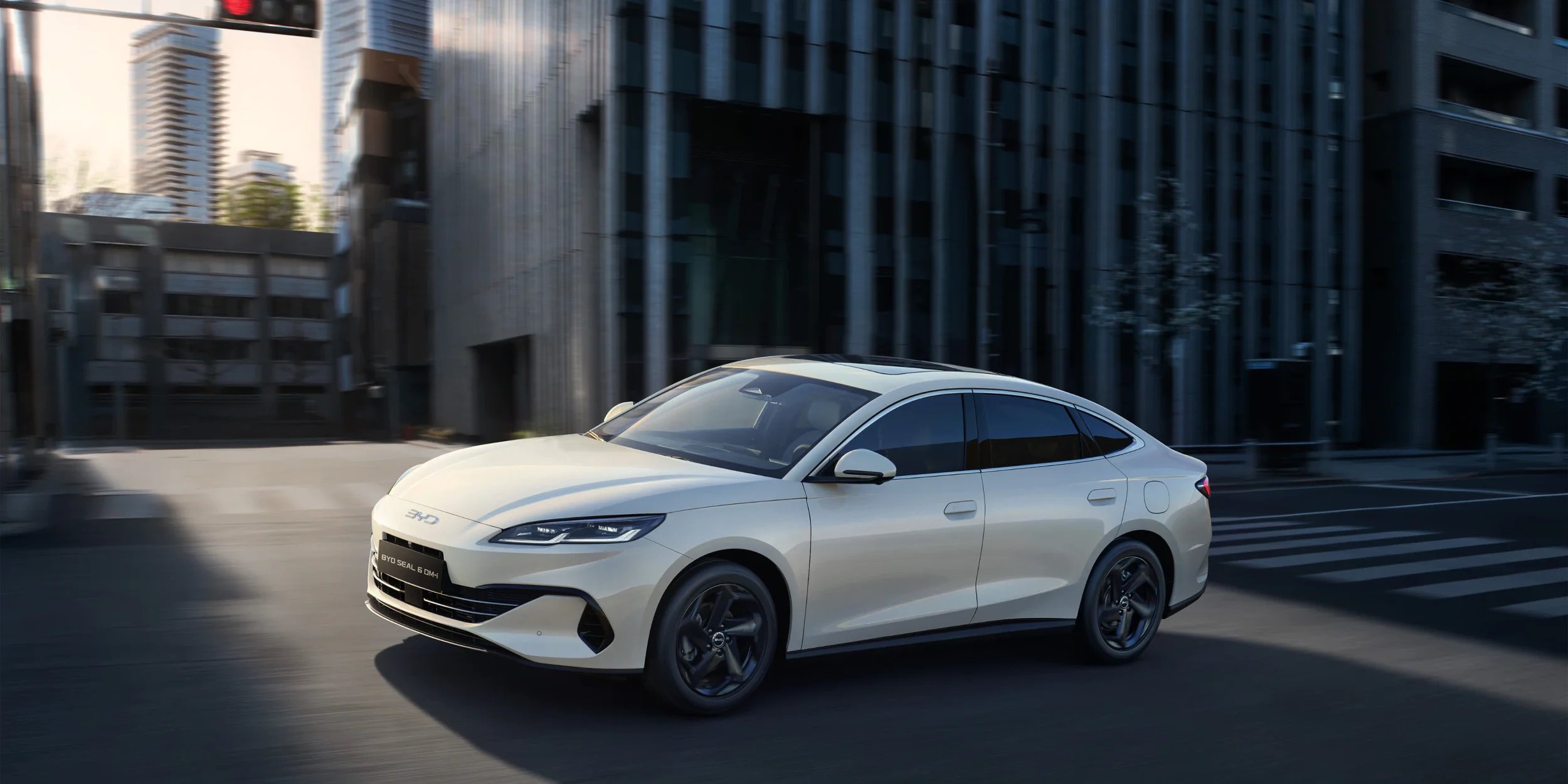 Biały samochód hybrydowy BYD Seal 6 DM-i Sedan jadący ulicą w nowoczesnym mieście.