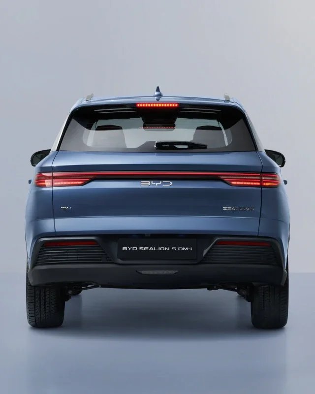 Niebieski hybrydowy SUV BYD Sealion 5 DM-i sfotografowany od tyłu na jednolitym, jasnoszarym tle, prezentujący pas świetlny LED, centralne logo BYD oraz oznaczenia modelu na klapie.