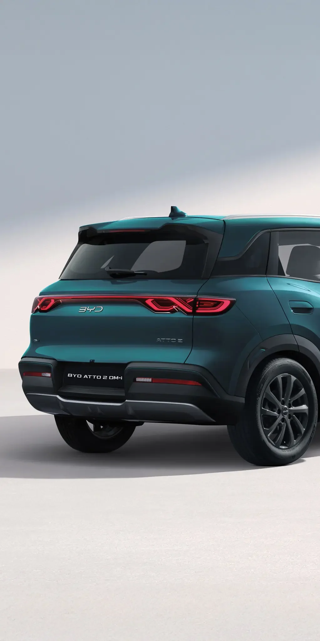 Zbliżenie na tył hybrydowego SUV-a BYD Atto 2 DM-i w turkusowym lakierze, przedstawiające tylną szybę ze spoilerem, pas świetlny LED oraz lewe tylne koło na jasnym tle.