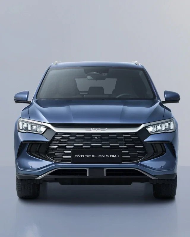 Niebieski hybrydowy SUV BYD Sealion 5 DM-i sfotografowany na wprost na jednolitym, jasnoszarym tle, prezentujący duży przedni grill, reflektory LED oraz logo marki.