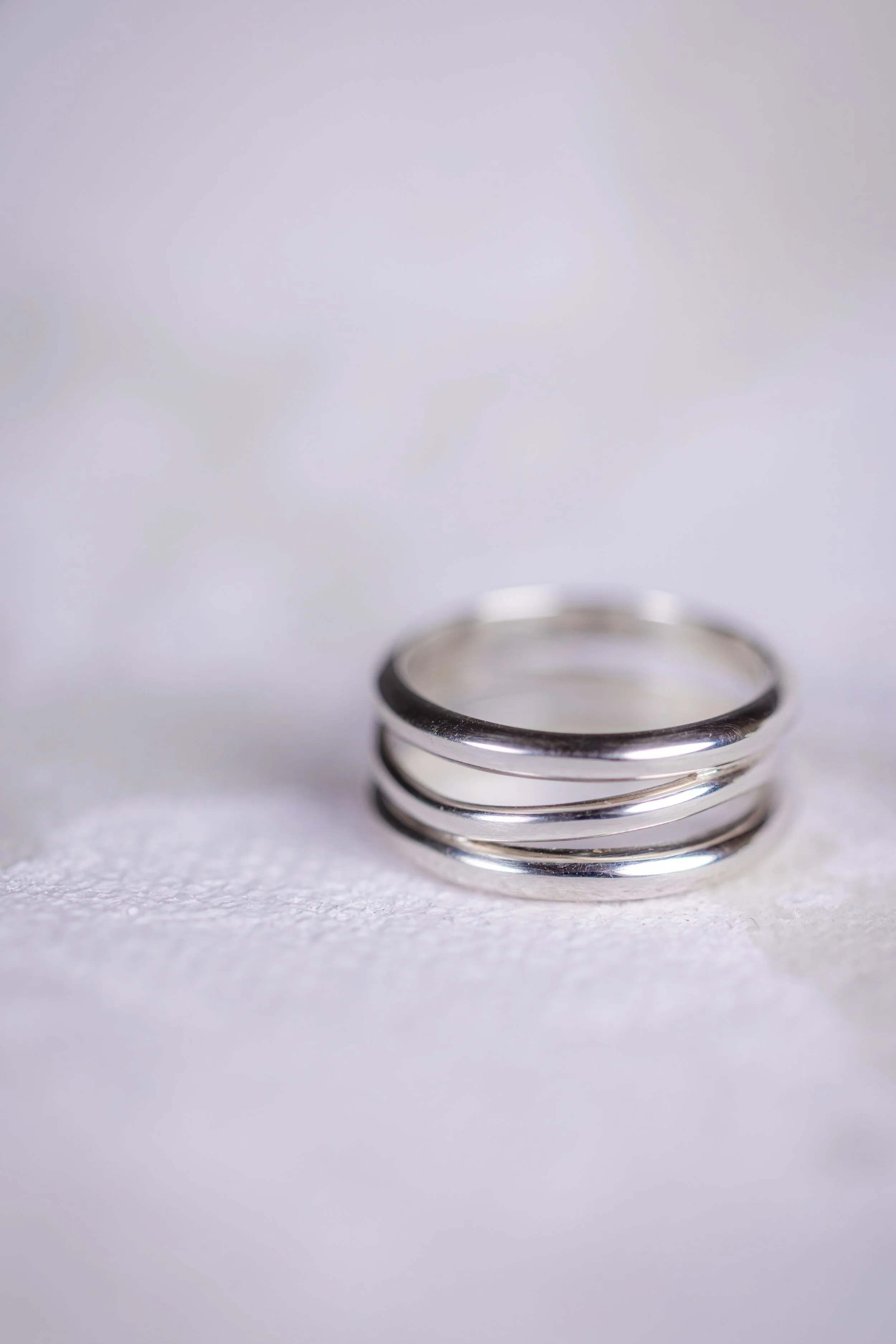 Une bague en argent composée de trois cercles, posée sur une surface blanche.