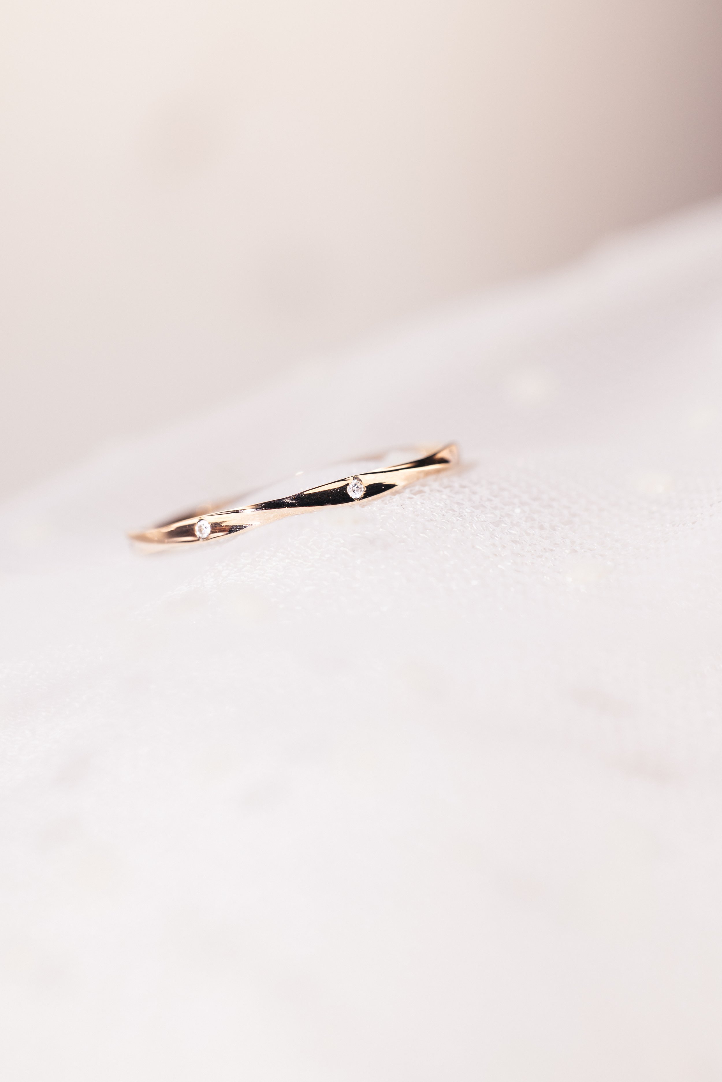 Alliance torsadée en or rose sertie de tout petit diamants éthiques posée sur un voile de mariée