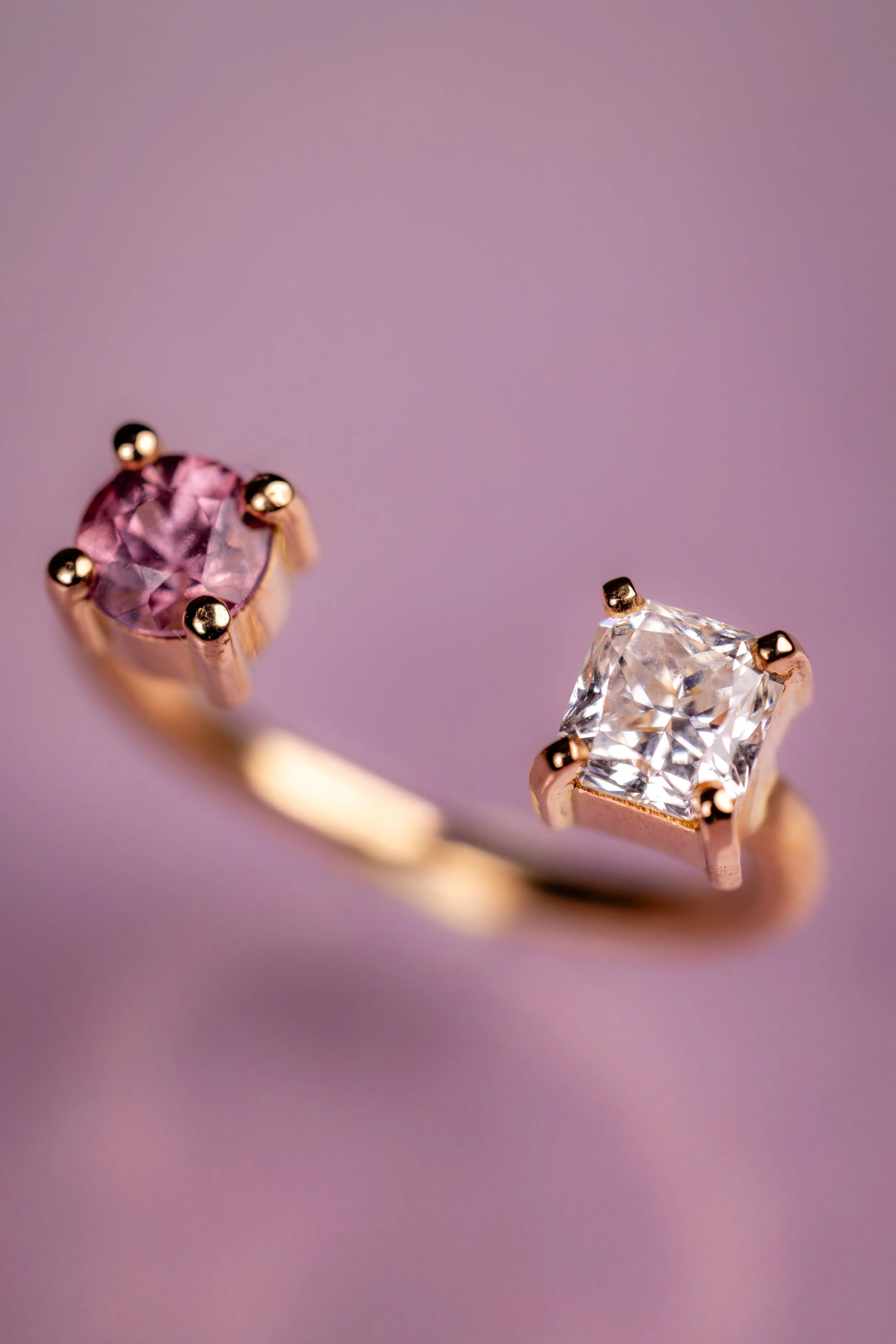 Une bague ornée de deux pierres précieuses, une grenat malaya et un diamant korloff, placé contre un fond rose claire.