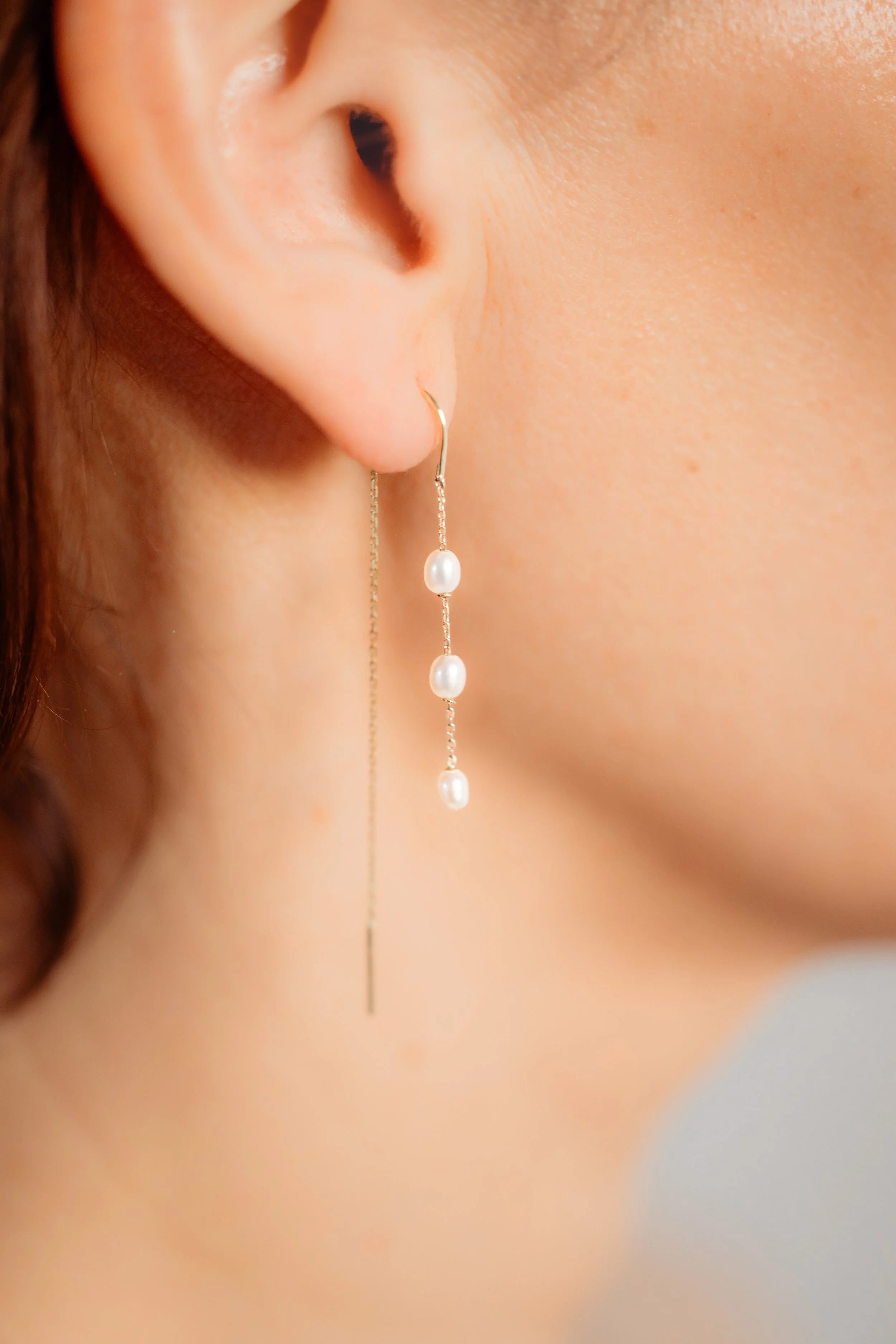 Boucle d'oreille pendante avec trois perles blanches et une chaîne fine en métal.