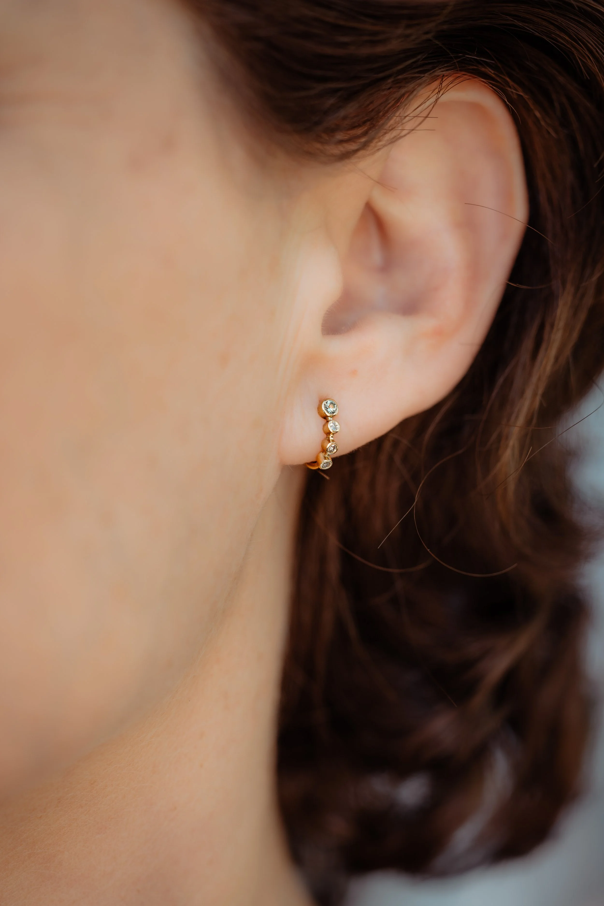 Une femme porte une boucle d'oreille en or avec plusieurs petits diamants.