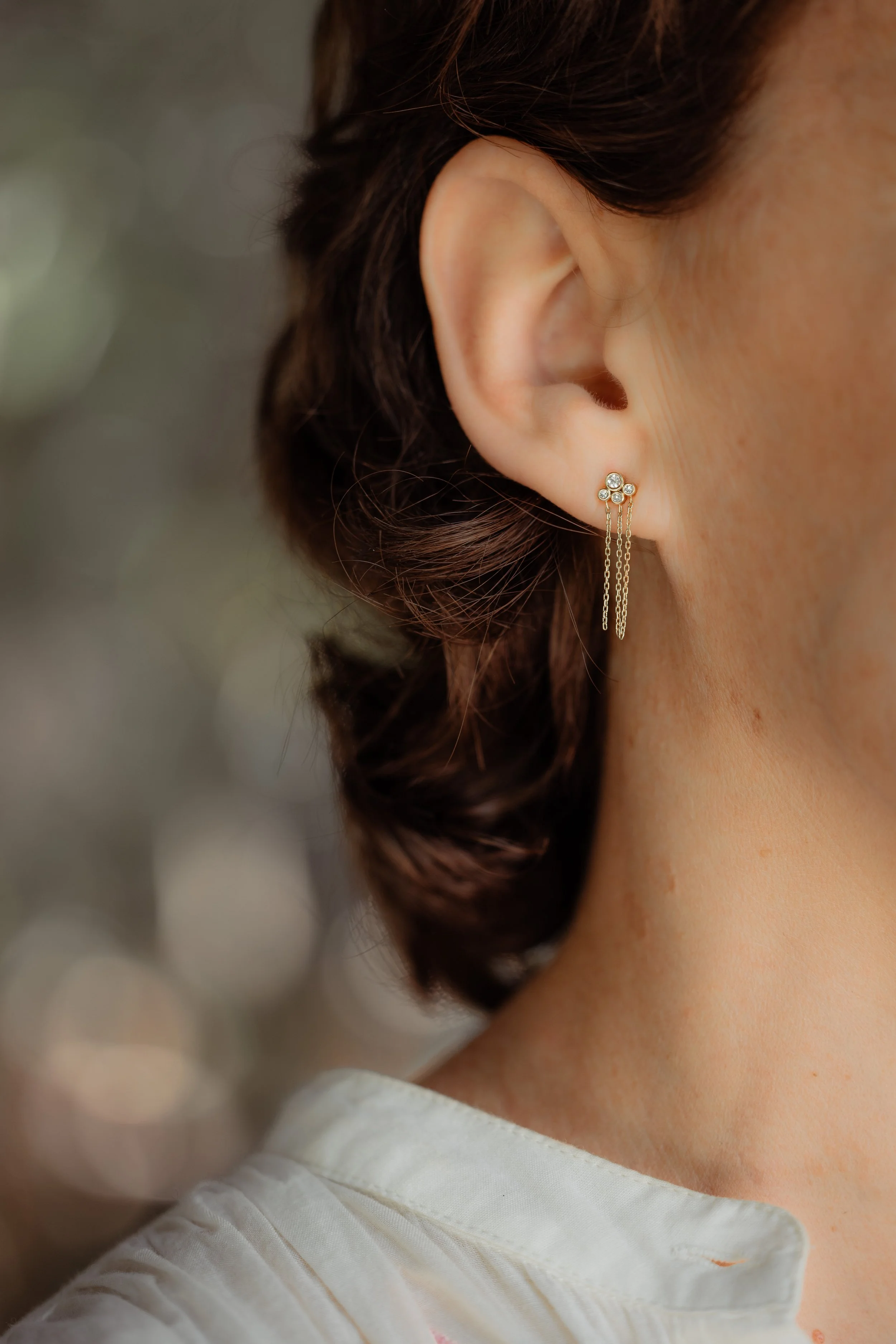 Une oreille d'une femme avec une boucle d'oreille dorée à trois diamants avec des chaînes fines suspendues