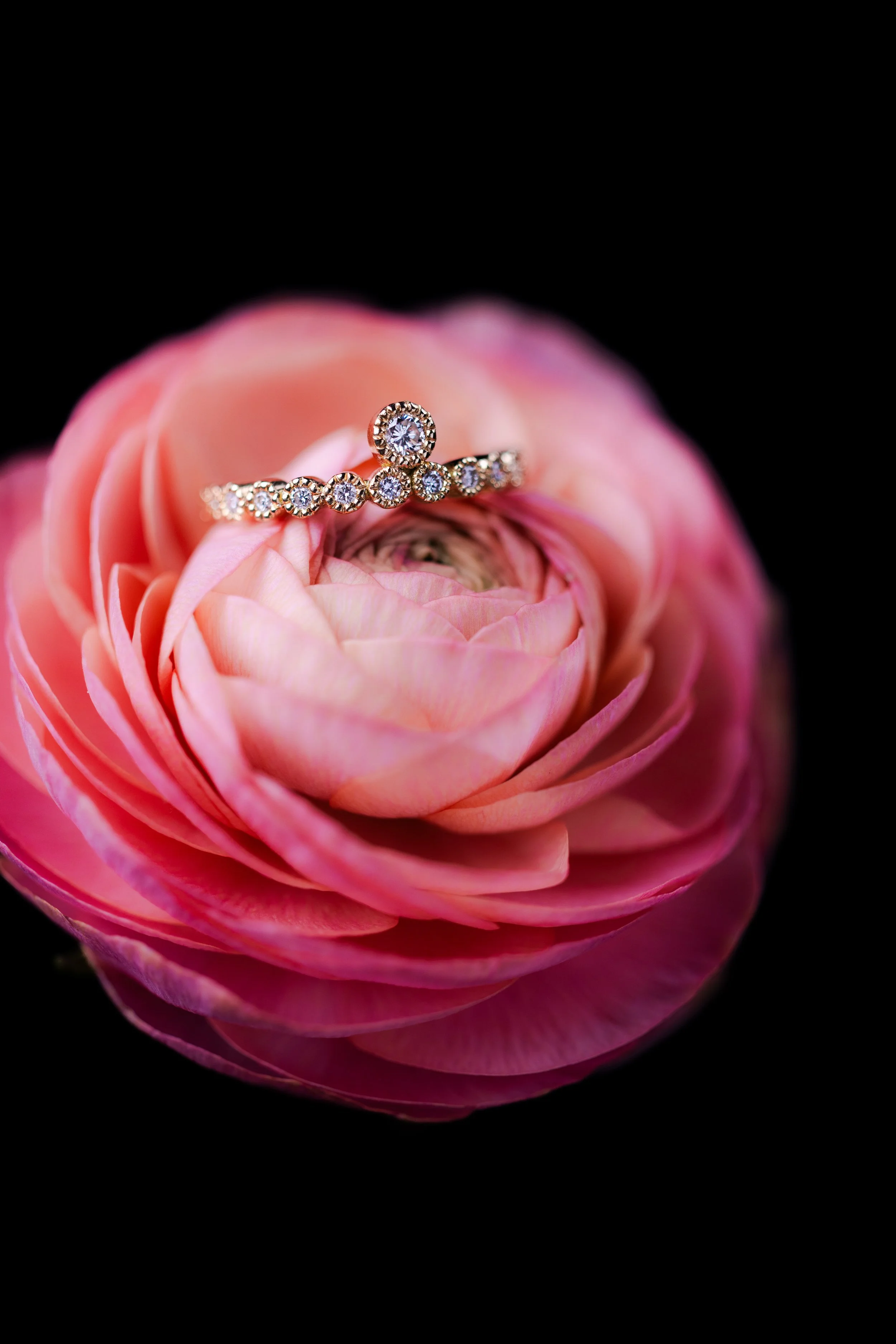 Une bague en or avec des diamants posée sur une fleur rose.