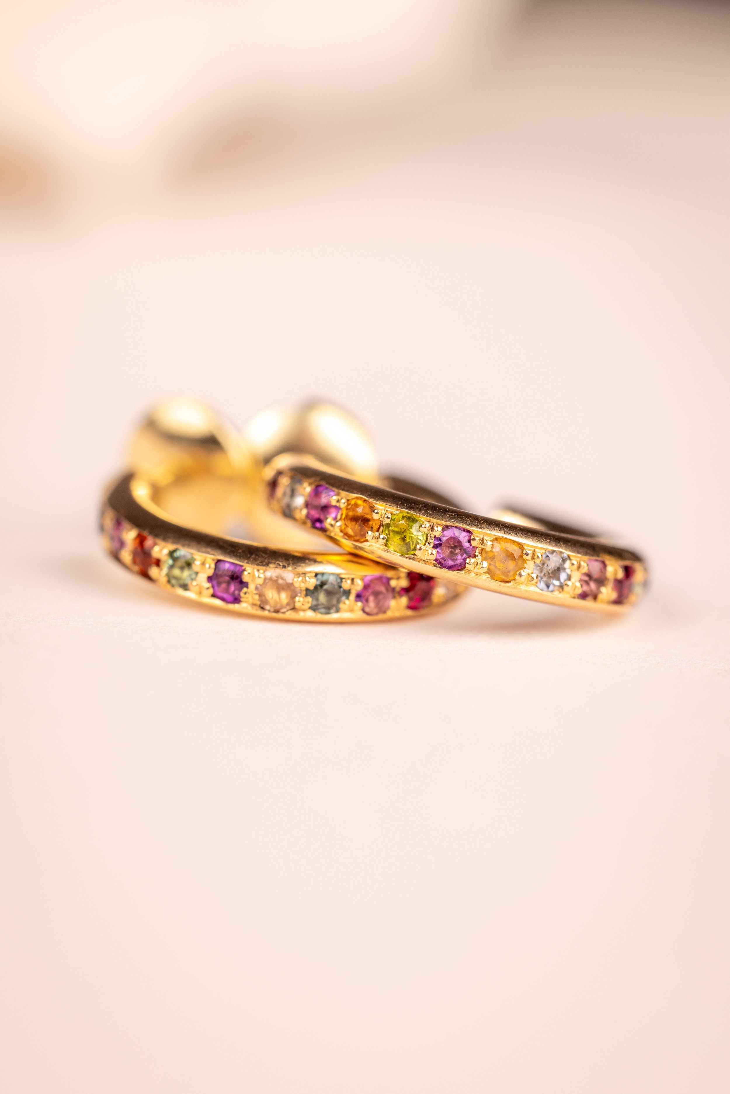 Paire de boucles d'oreilles en or ornées de pierres précieuses colorées, posées sur une surface claire.