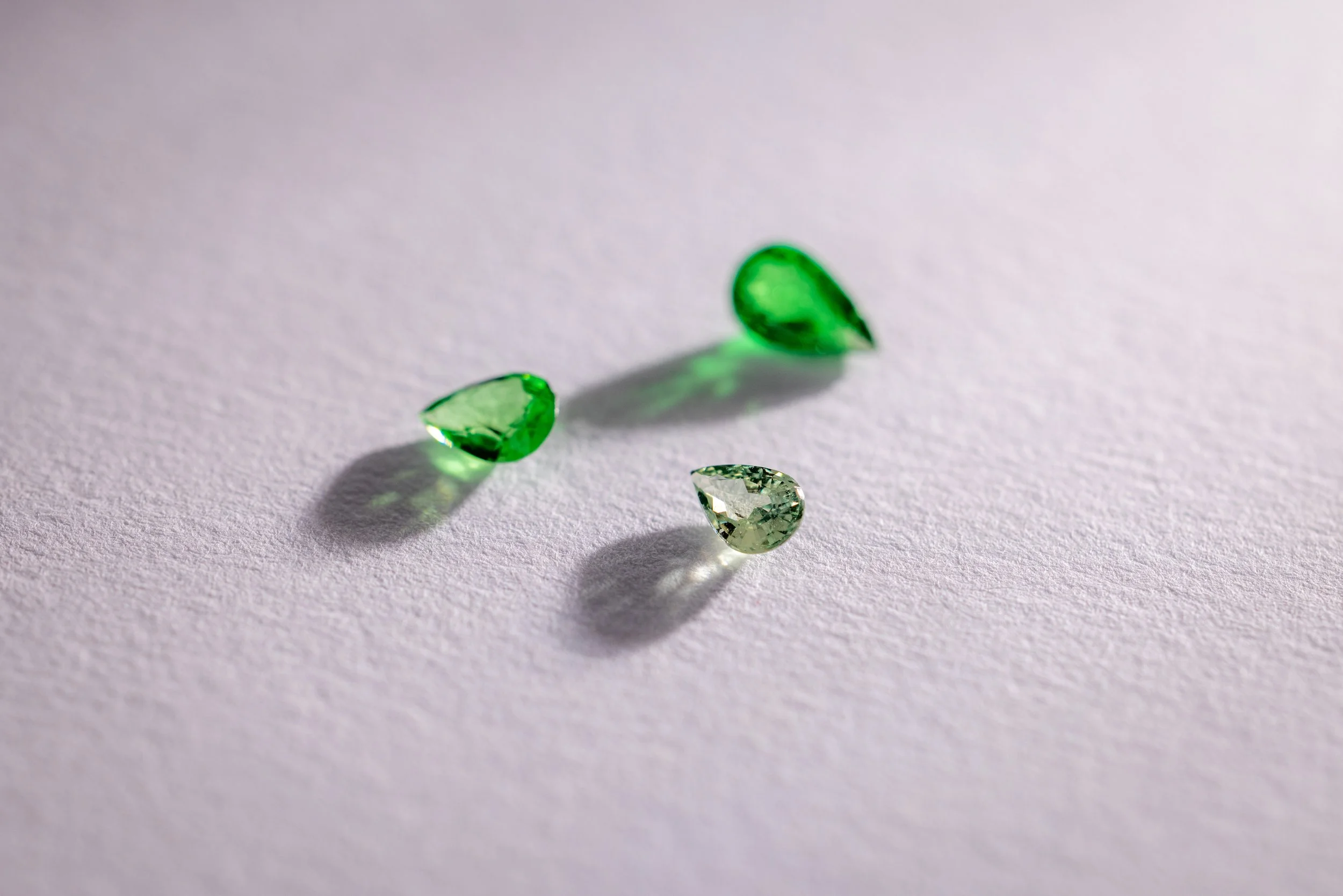 Trois tsavorites sur une surface blanche avec ombres.