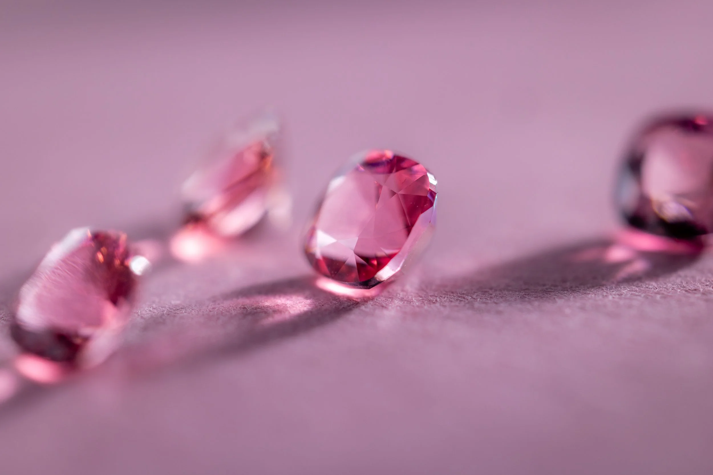 Des pierres précieuses roses disposées sur une surface de couleur rose. La pierre centrale est en focus, d'autres pierres sont floues à l'arrière-plan.