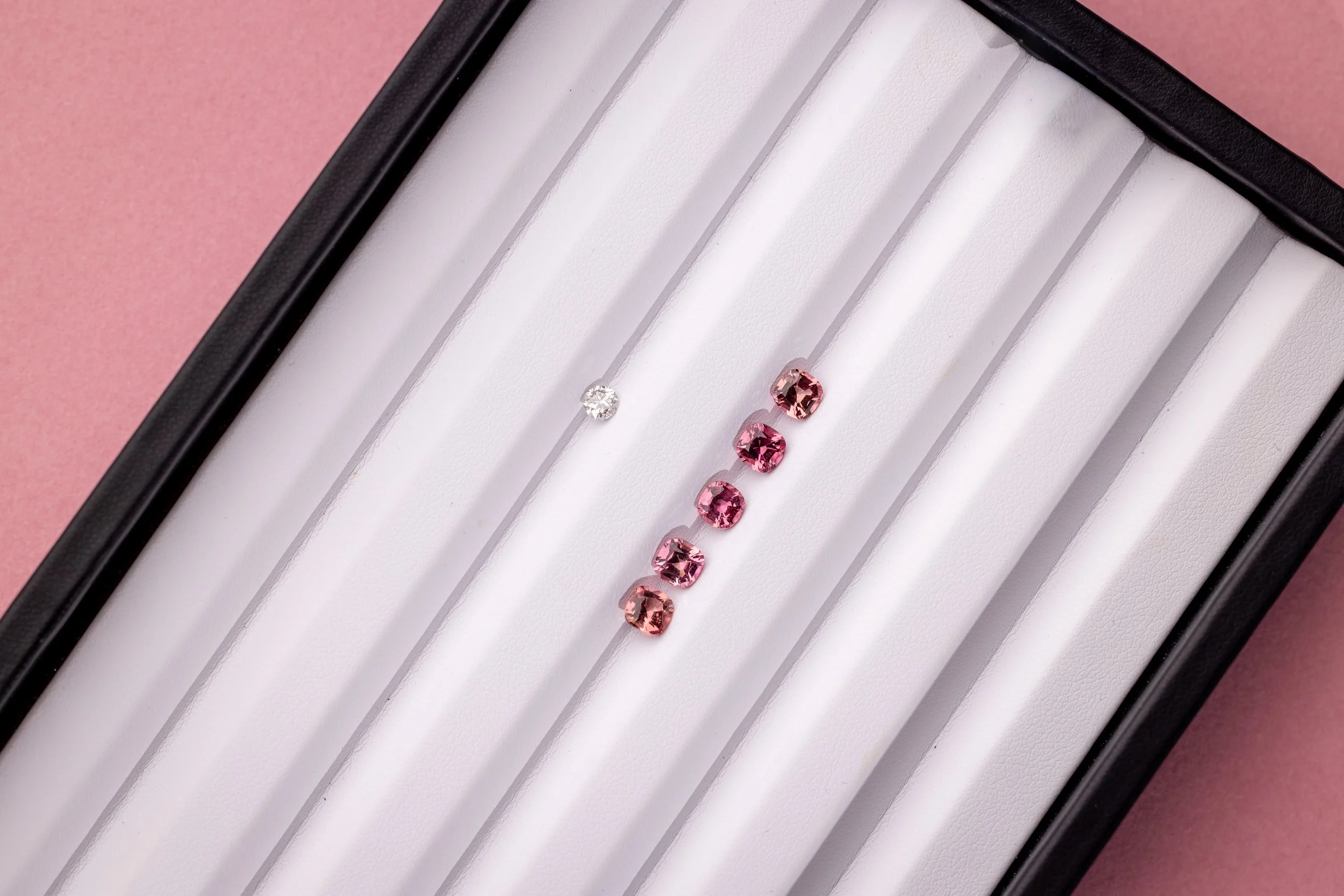 Une boîte contenant cinq tourmalines roses et un diamant, disposés de gauche à droite.
