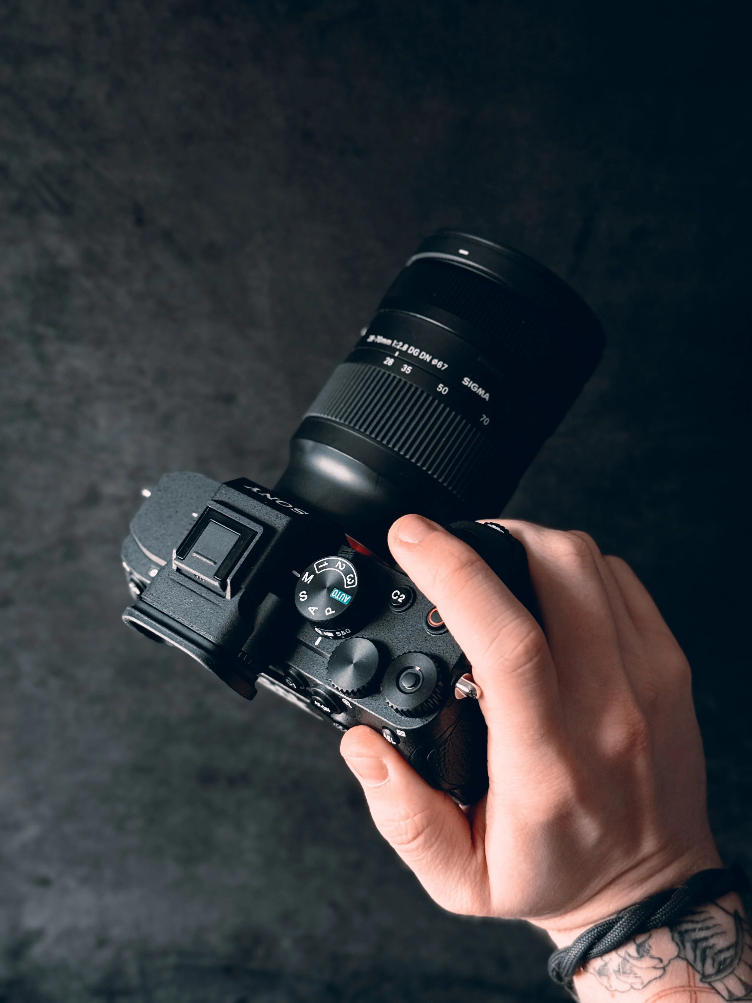 Close-up of a person's hand holding a black Sony camera with a Sigma lens against a dark background.
