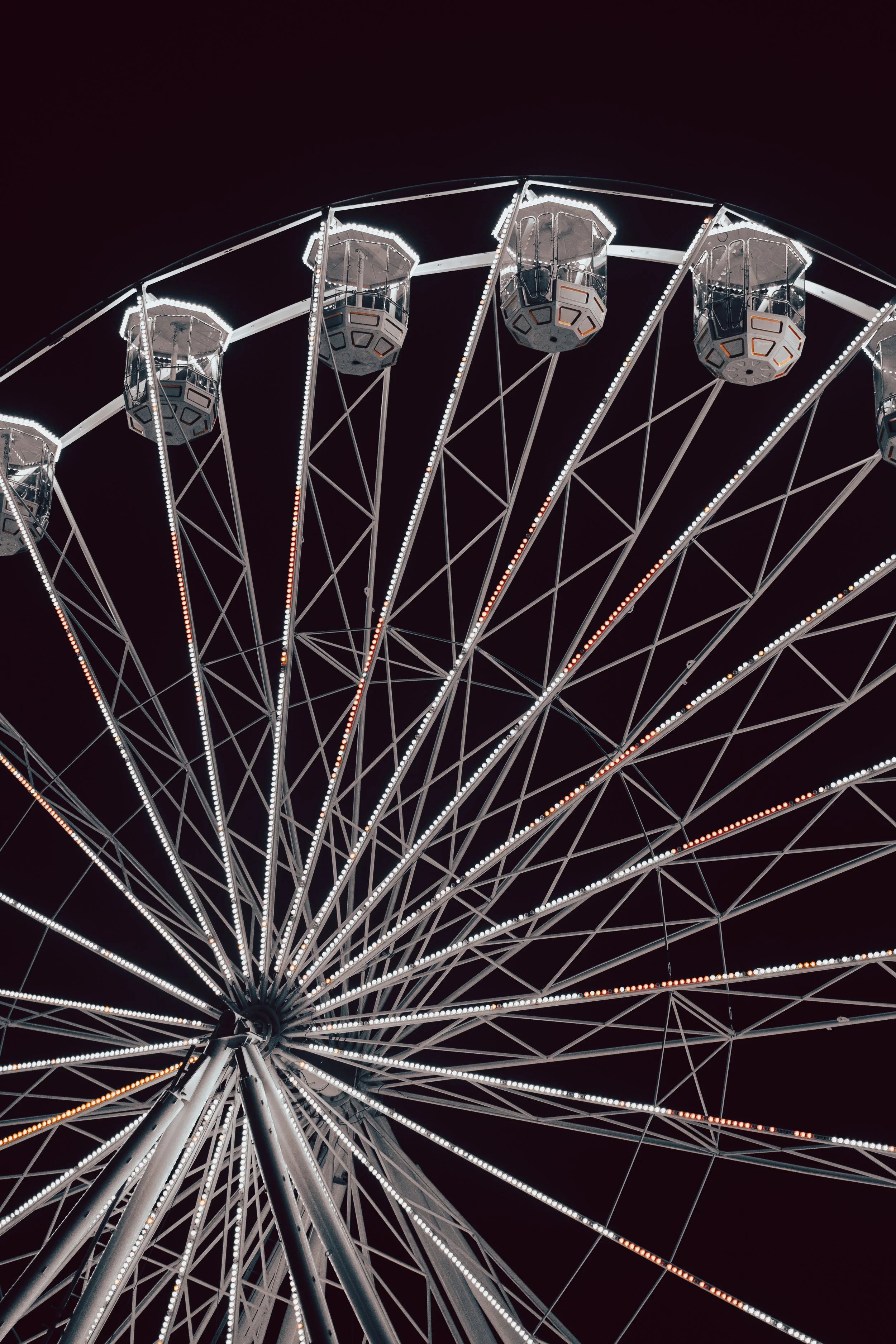 Night view of a lit Ferris wheel with enclosed gondolas against a dark sky.