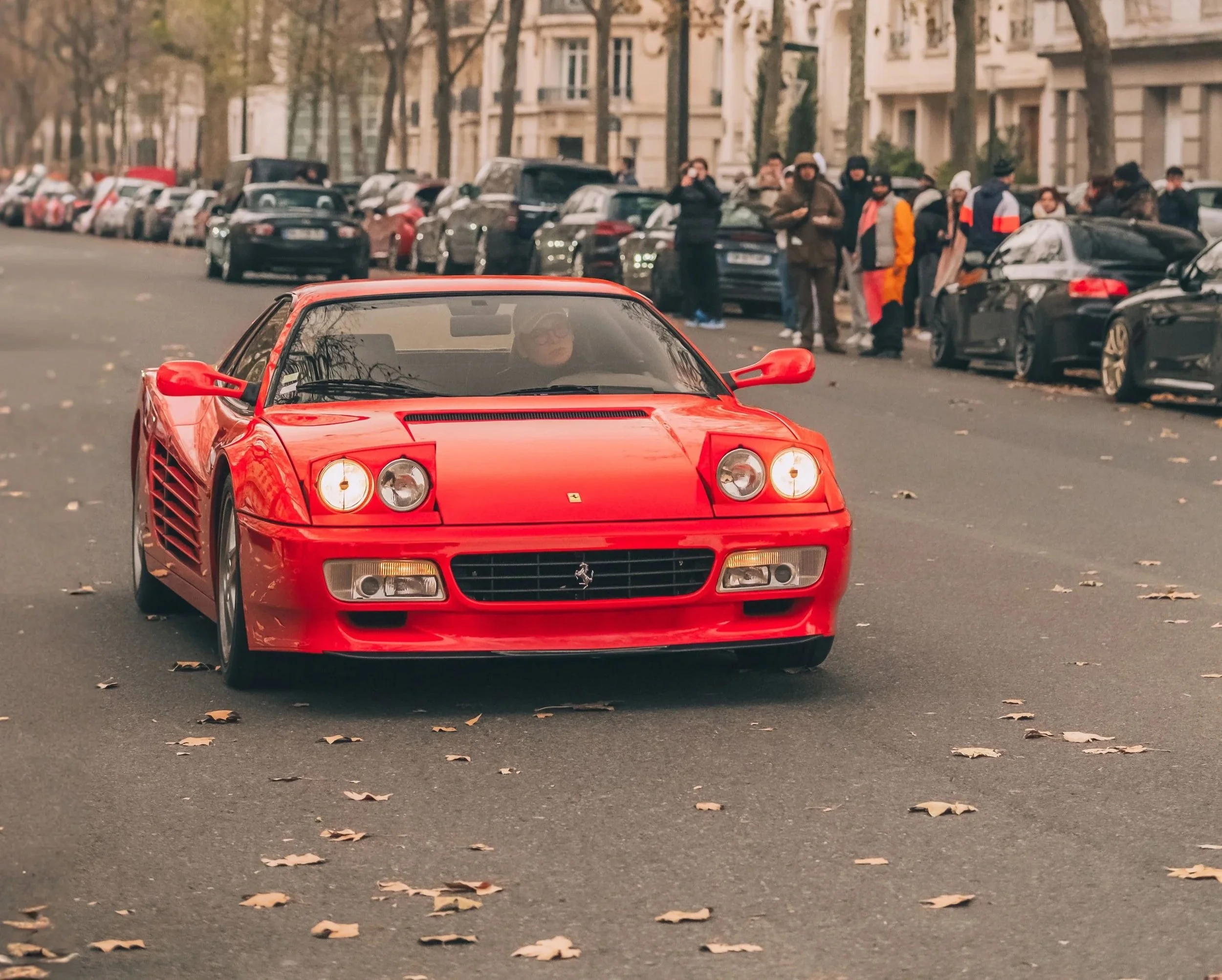 Voiture Ferrari rouge sur une rue urbaine avec des personnes et d'autres voitures en arrière-plan.