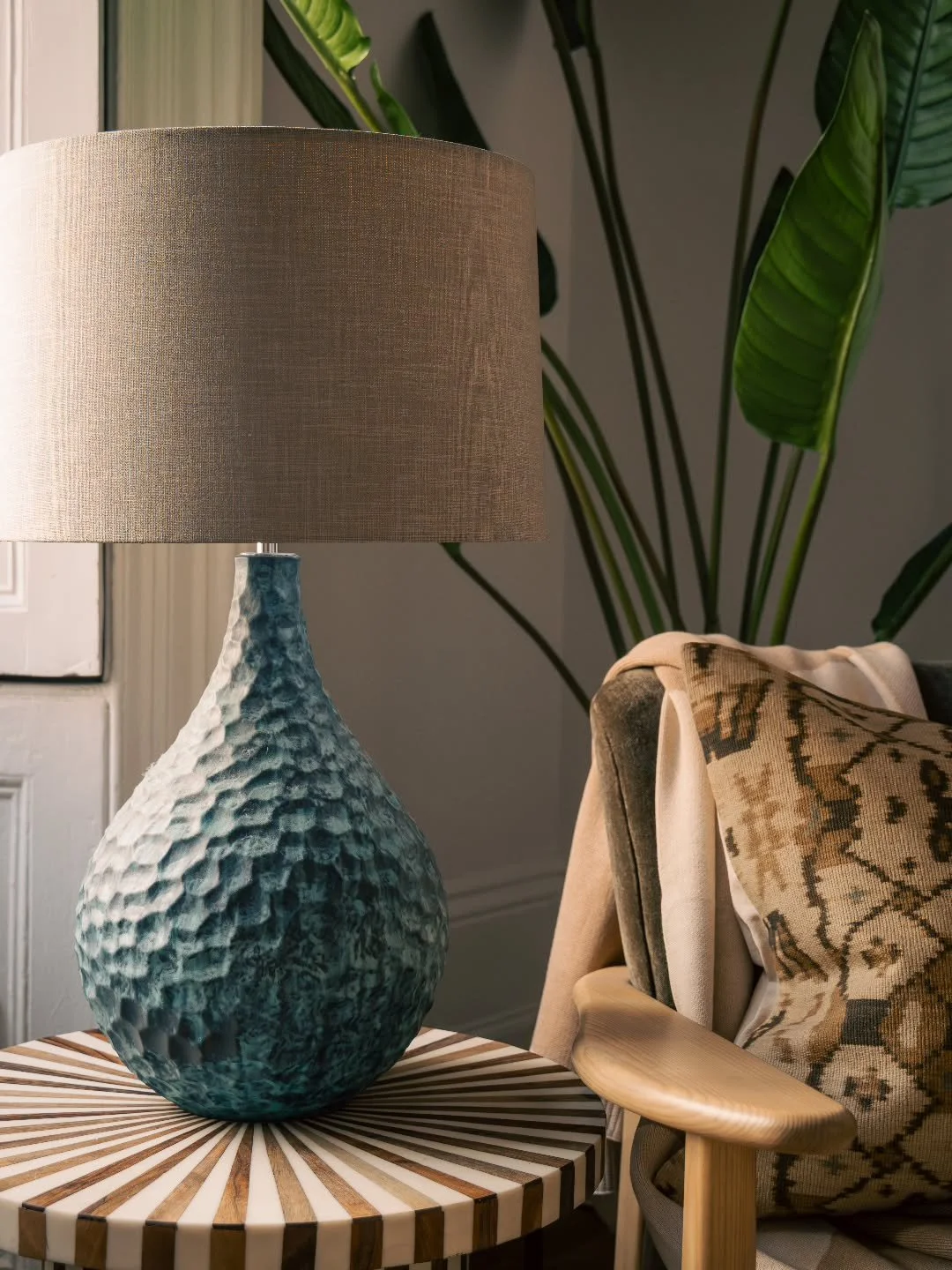 Layering is all about balancing texture, pattern, height, and colour to create a cohesive space. In this quiet corner of a formal living room we designed the handcrafted grooved lamp, striped resin inlay table, softly patterned textiles, and timber-f