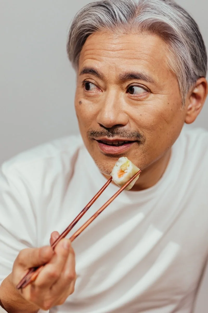 Homme heureux qui mange des sushis avec une paire de baguettes.