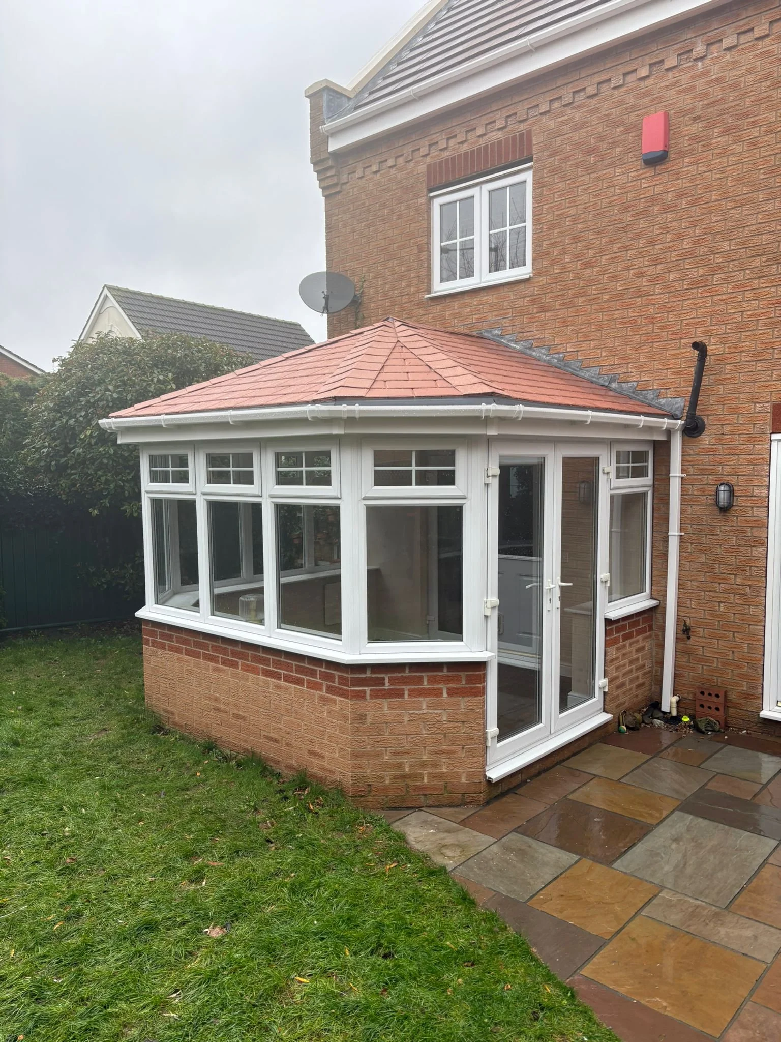 A brick house with a white enclosed porch, a small window above, and a patio with stone tiles outside.