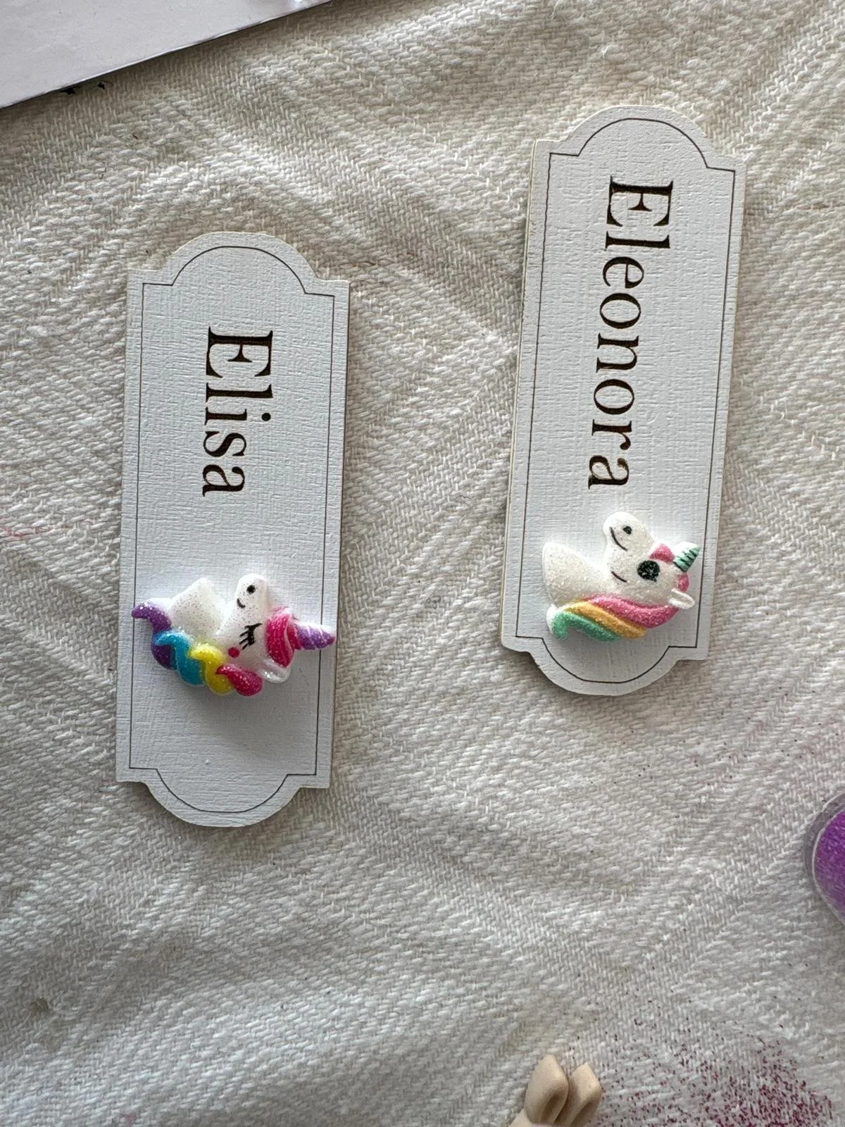 Inserto con etichette con scritte in italiano, una dice 'Eisa' e l'altra 'Beonja', ciascuna con una decorazione a forma di unicorno colorato.