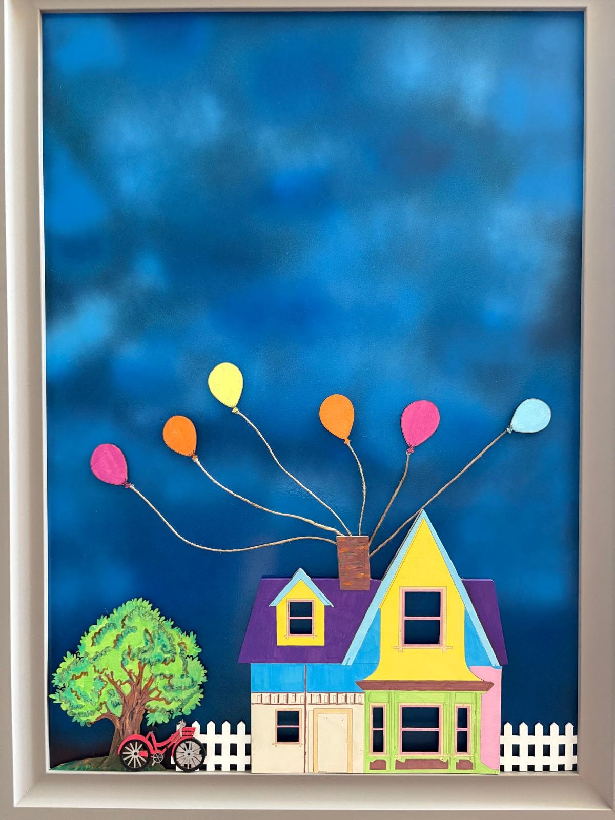 Una casetta colorata con un albero e una bicicletta di fronte, con palloncini colorati che volano nel cielo
