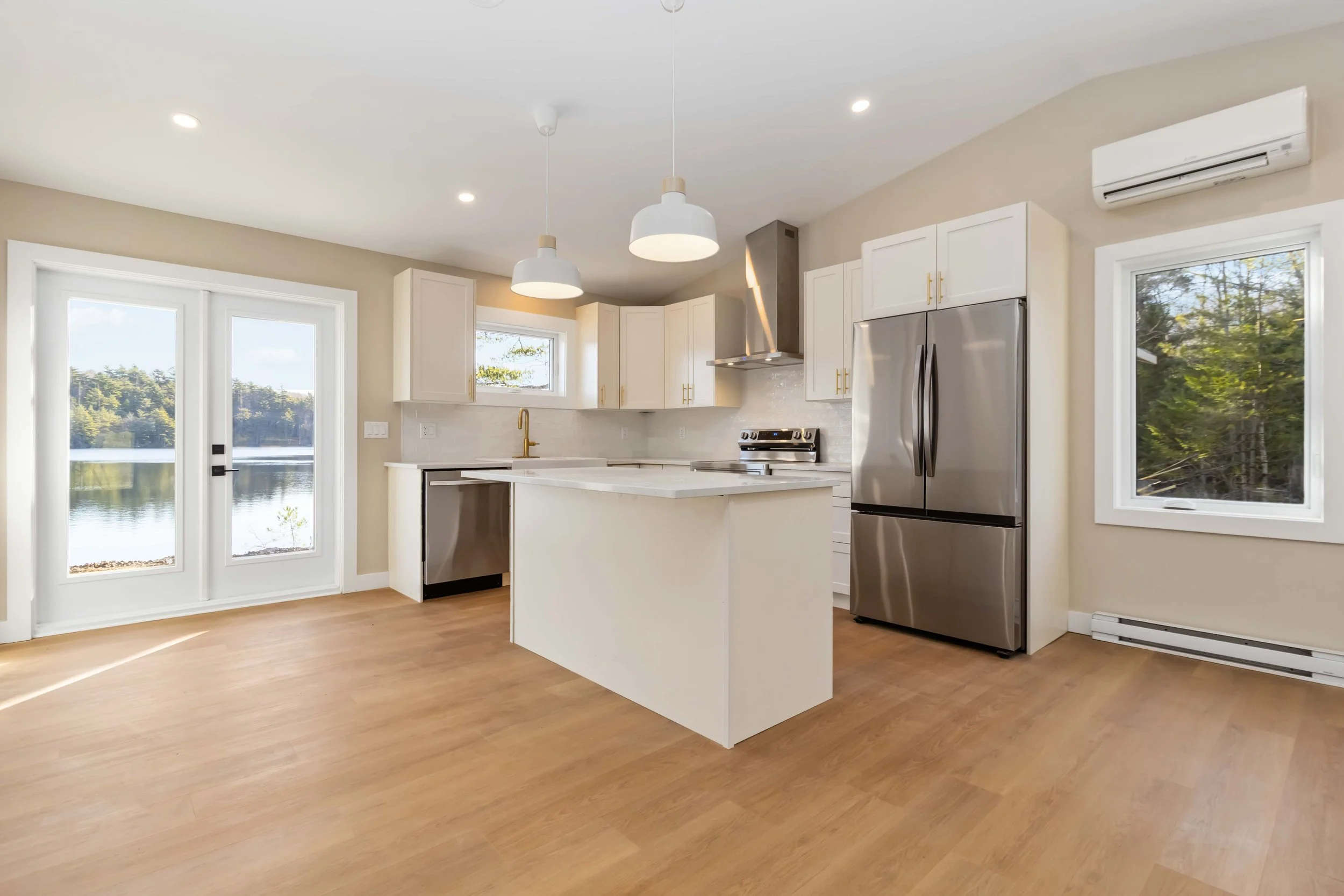 Modern kitchen with white cabinets, stainless steel appliances, large windows, light wood flooring, and pendant lighting.