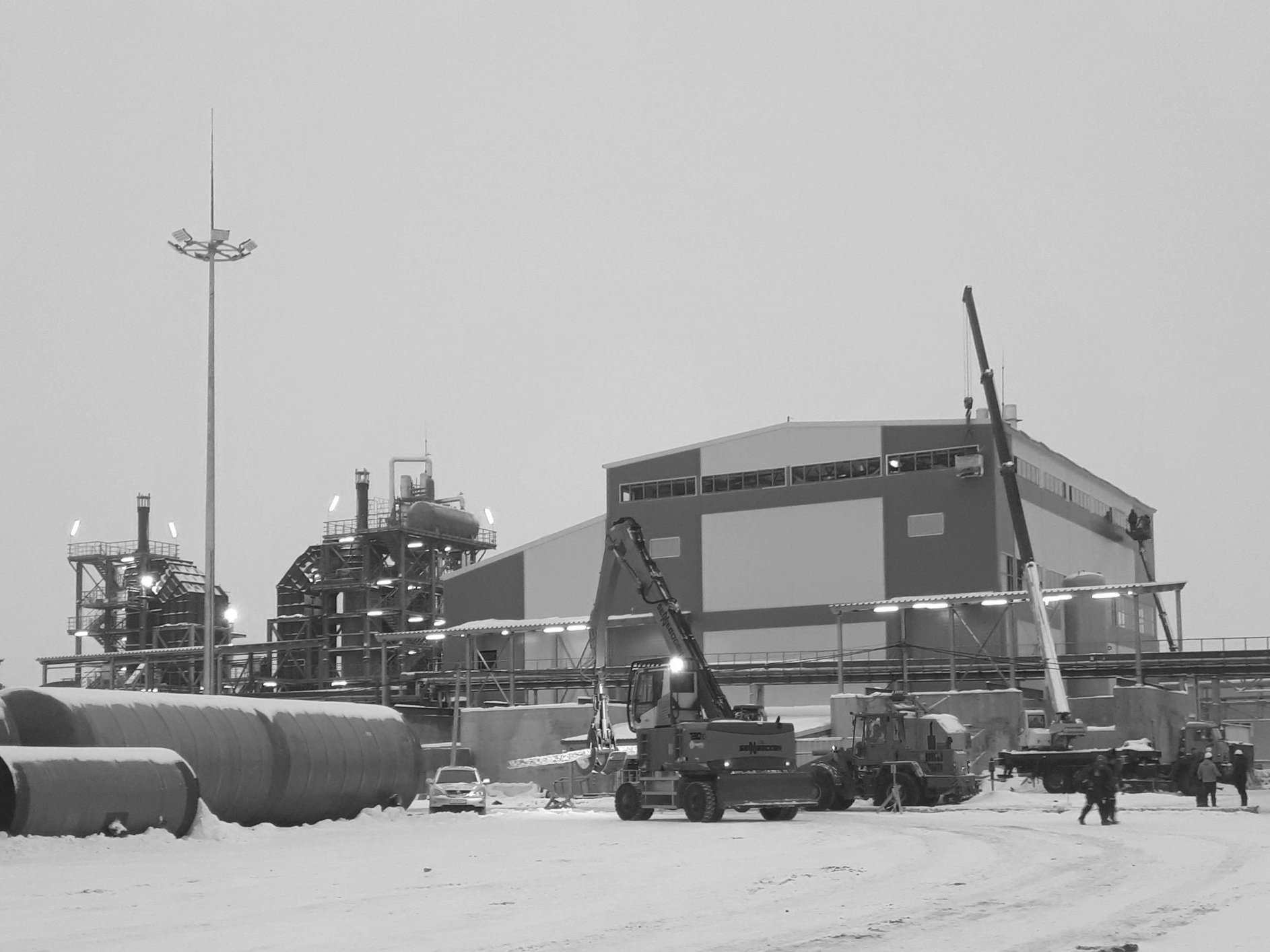 Industrial site with large building, cranes, and heavy machinery on a snowy day.