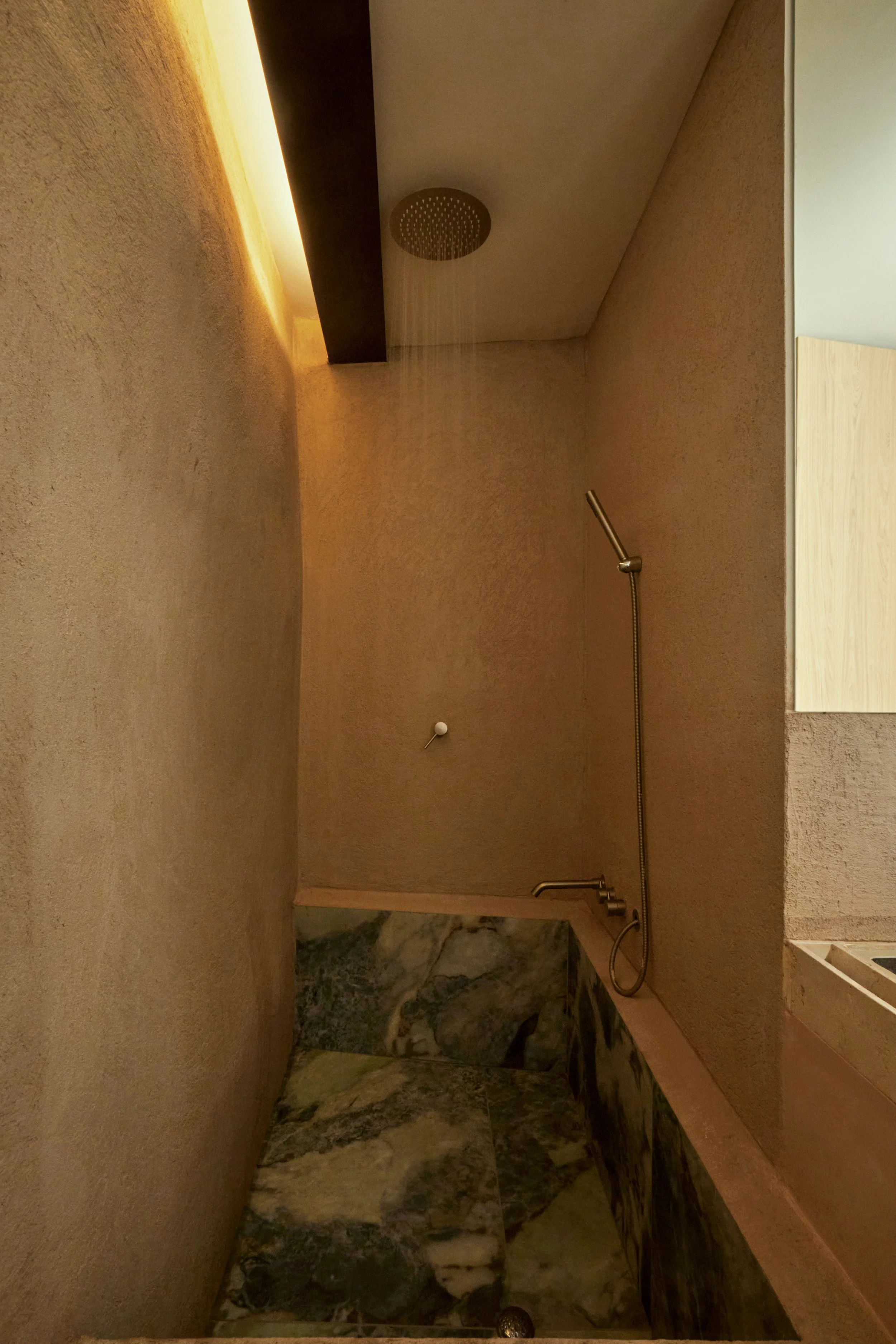 Douche minimaliste aux matières texturées dans cette maison rénovée à Marseille par Local Club. Les enduits minéraux, la pierre sombre et l’éclairage indirect créent une atmosphère immersive, chaleureuse et contemporaine inspirée des bains méditerran