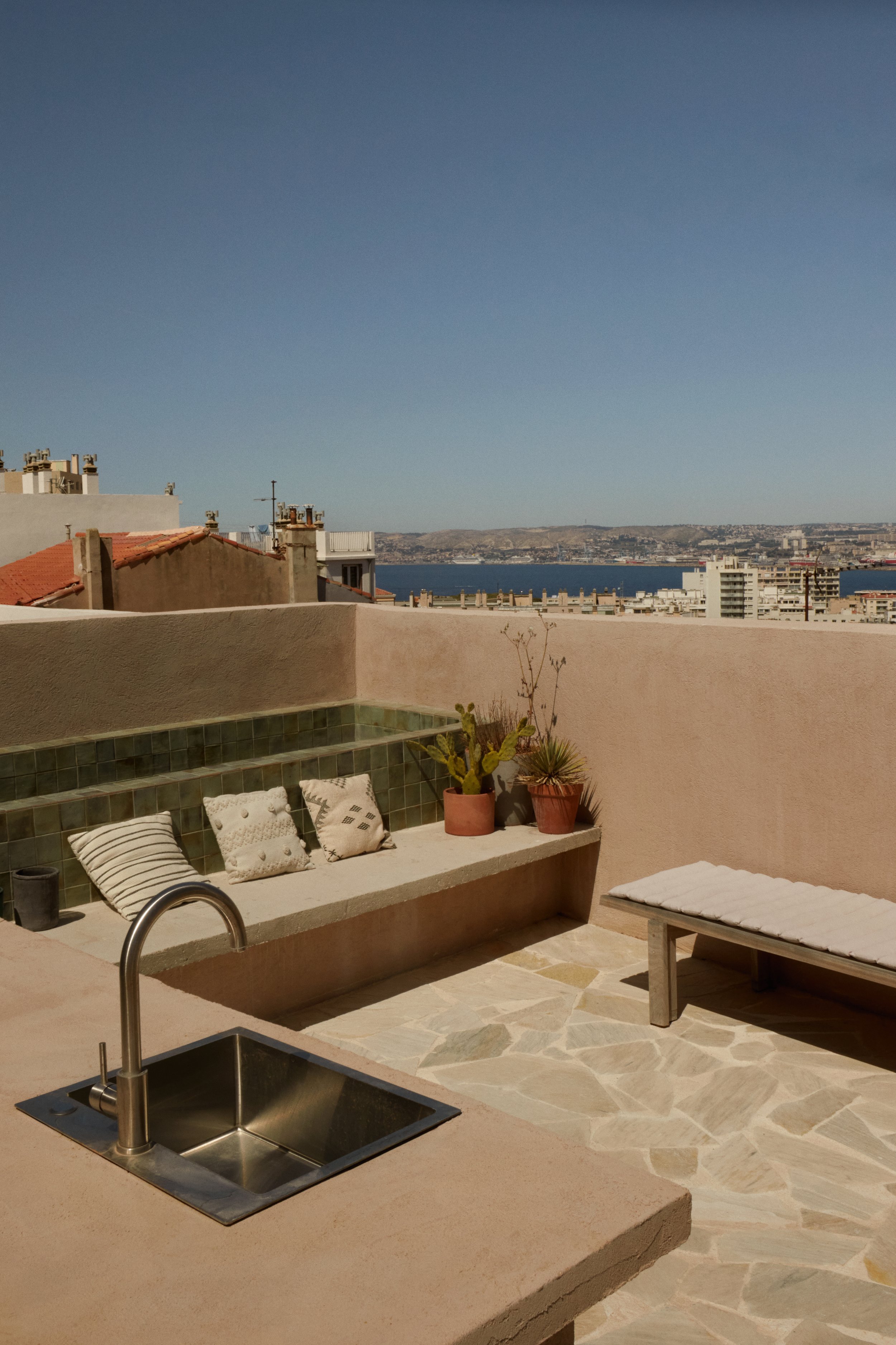 Rooftop minimaliste à Marseille avec vue panoramique sur la ville et la mer. Terrasse en pierre naturelle, banquette maçonnée, matières brutes et ambiance méditerranéenne contemporaine imaginées par Local Club.