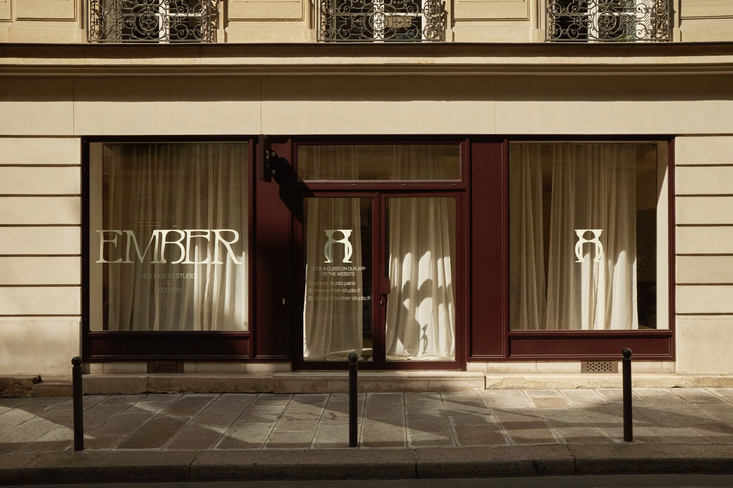 Façade d’un studio de sport et wellness à Paris, avec menuiseries brun-prune, vitrophanie sur mesure, rideaux et identité visuelle visible depuis la rue.