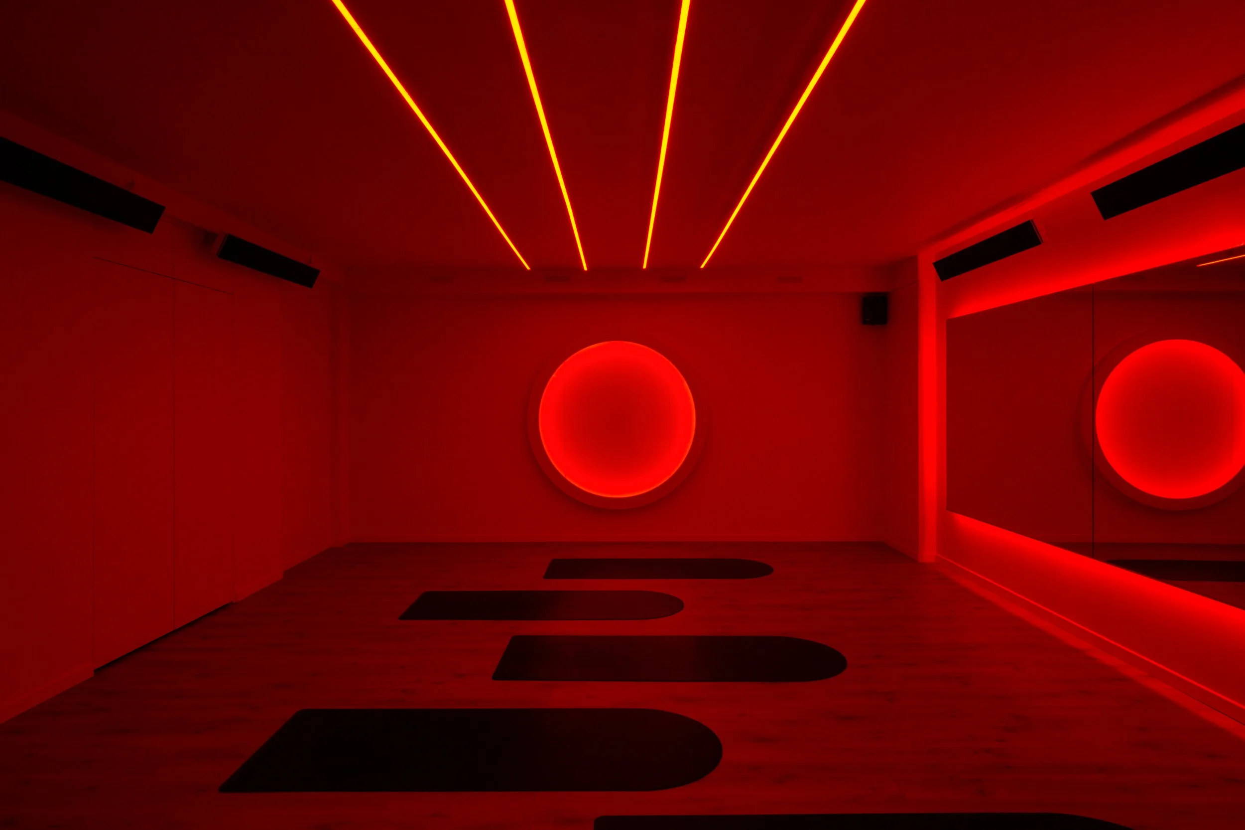 Design intérieur d’une hot room immersive pour studio de sport, Pilates ou yoga chaud, avec lumière rouge, miroirs, tapis et ambiance intense.