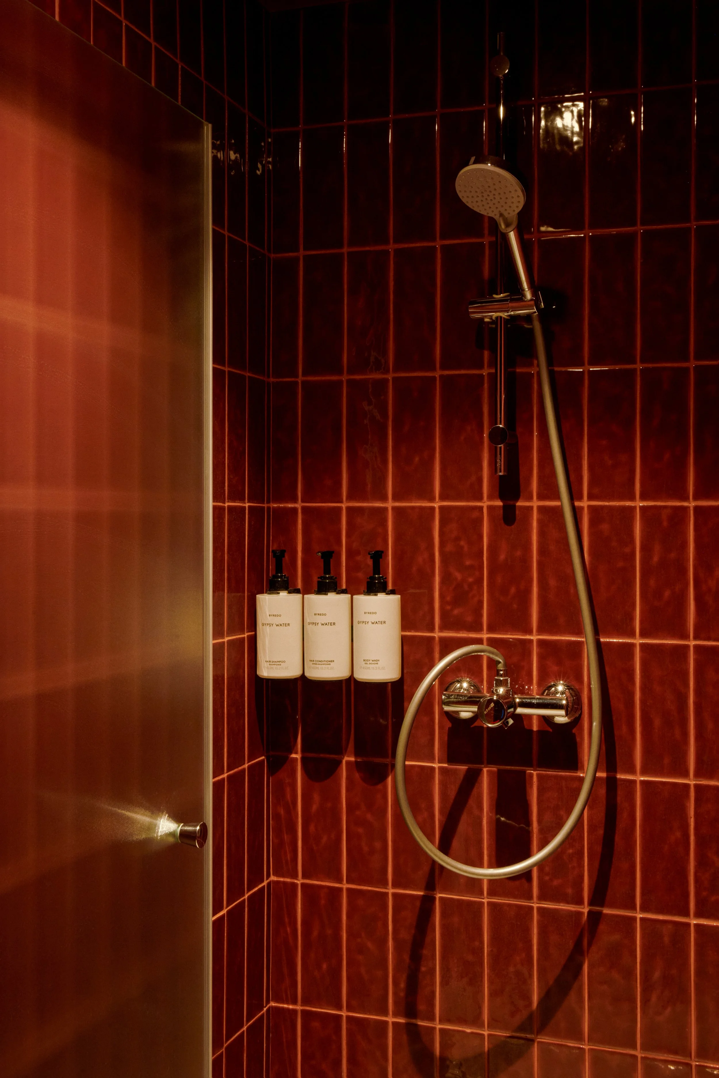 Détail d’une douche en carreaux rouges dans un studio wellness, avec choix des matériaux, équipements et ambiance chaude pensée pour l’expérience client.