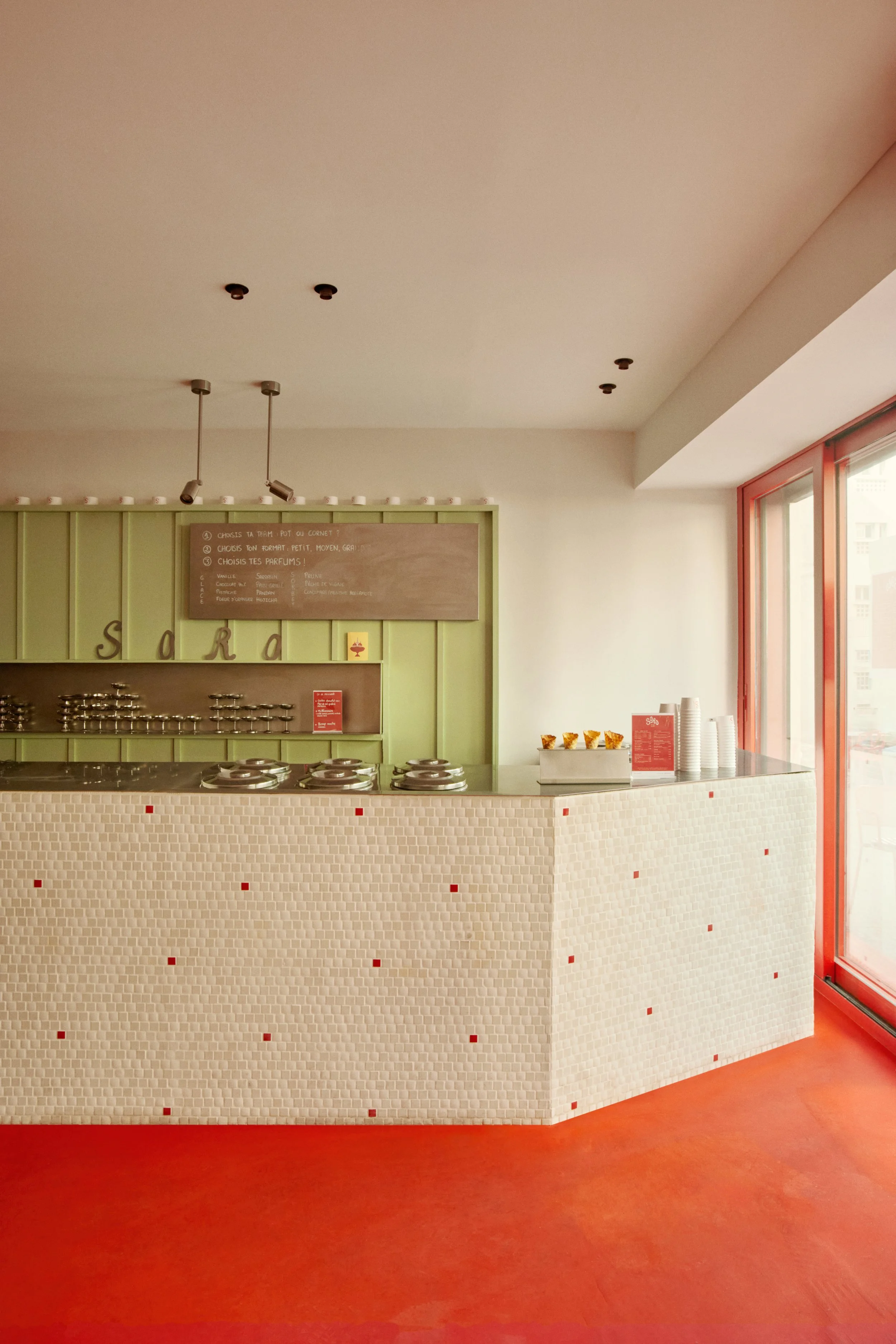 Comptoir du glacier SORO aux Catalans à Marseille, avec mosaïque crème, sol rouge fraise, menuiseries vert pistache et architecture intérieure signée Local Club.