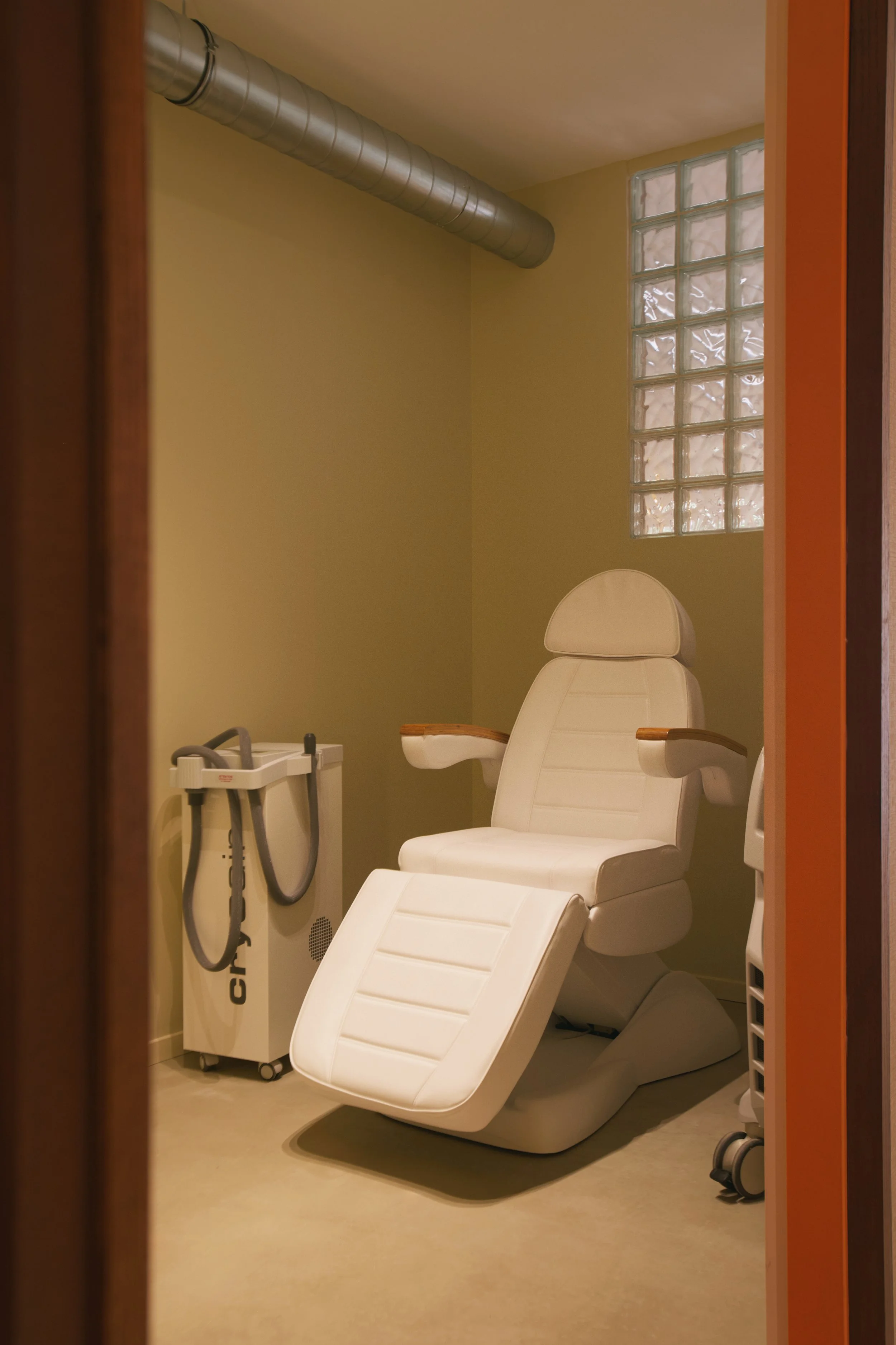 Salle de soin dans un centre de détatouage laser à Marseille conçue par Local Club. Architecture intérieure épurée, lumière douce et palette orange chaleureuse pour créer un environnement rassurant et maîtrisé.