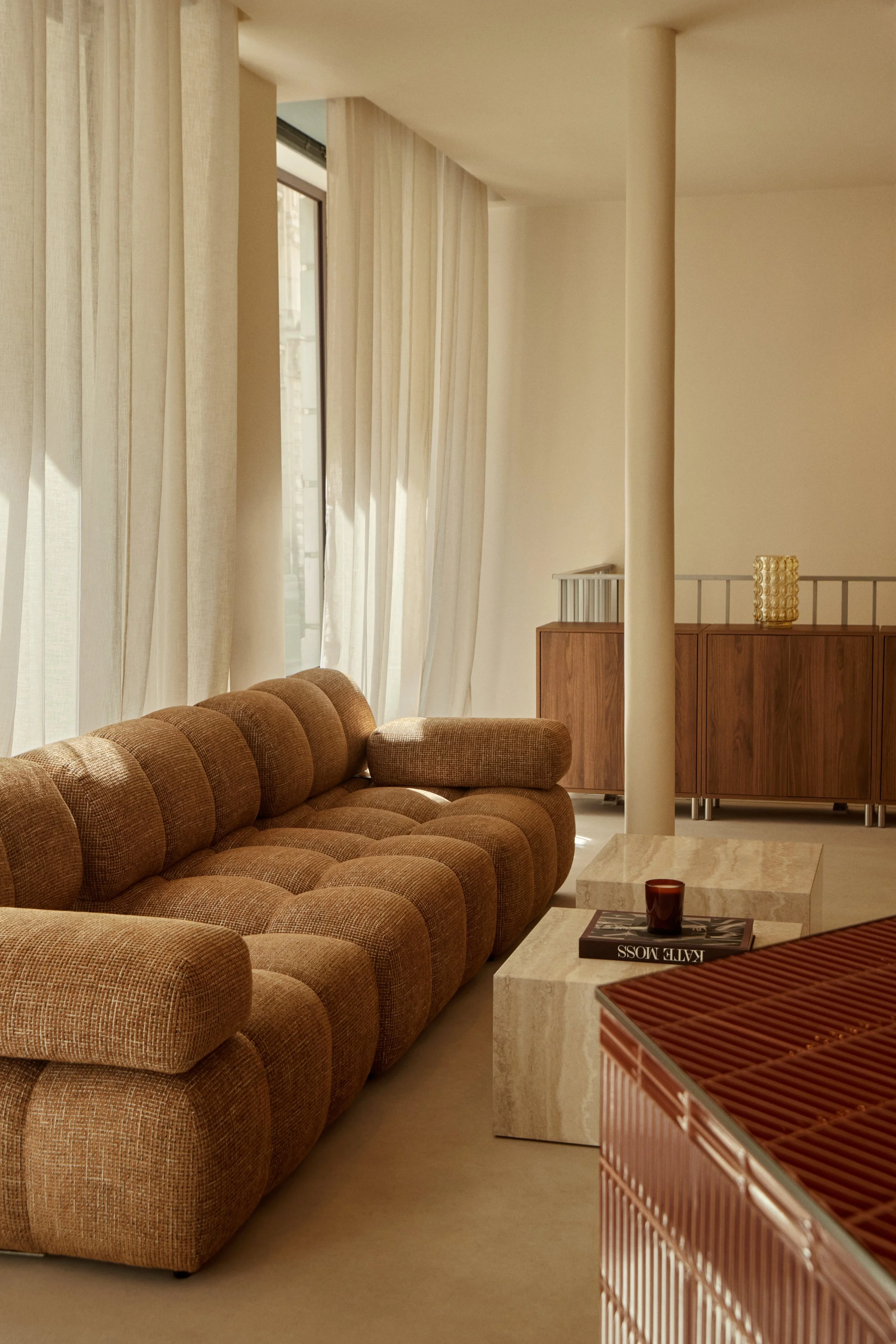 Aménagement intérieur d’un espace d’attente pour studio wellness, avec canapé texturé, tables effet pierre, rideaux et comptoir design.