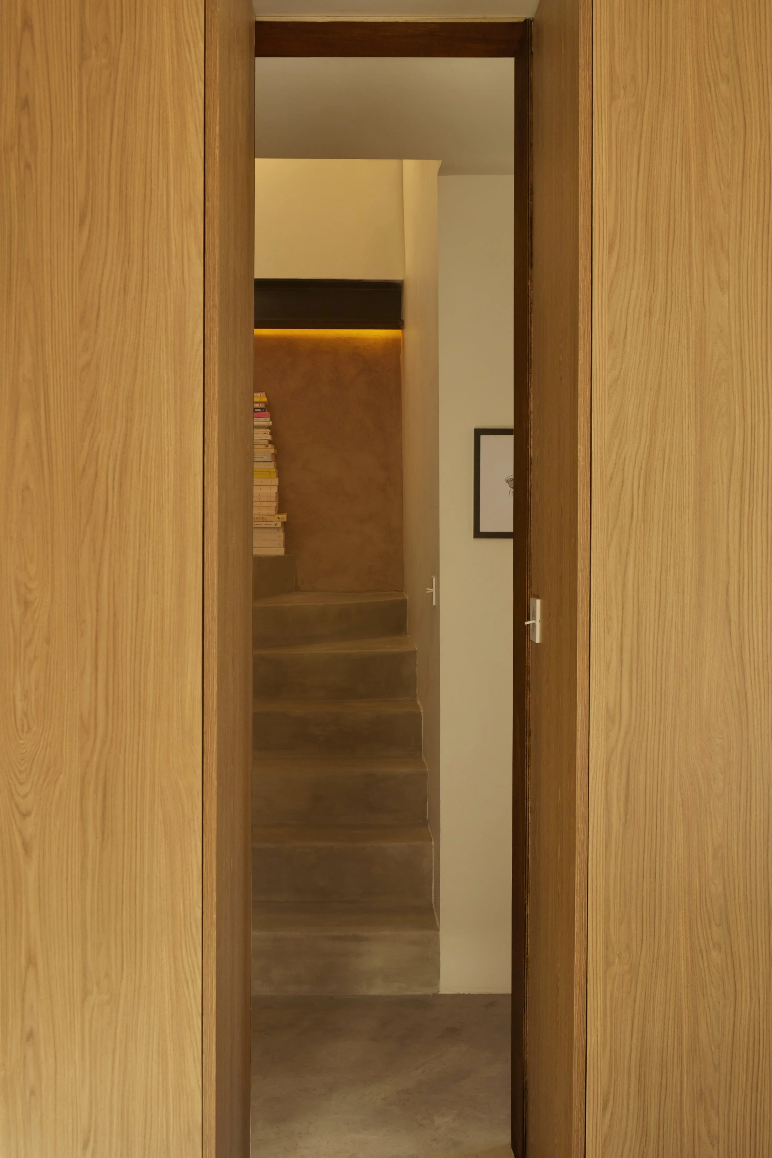 Perspective intérieure dans une maison rénovée à Samatan par Local Club. Dialogue entre béton ciré, bois sur mesure et lumière indirecte pour créer une circulation sobre et architecturée.