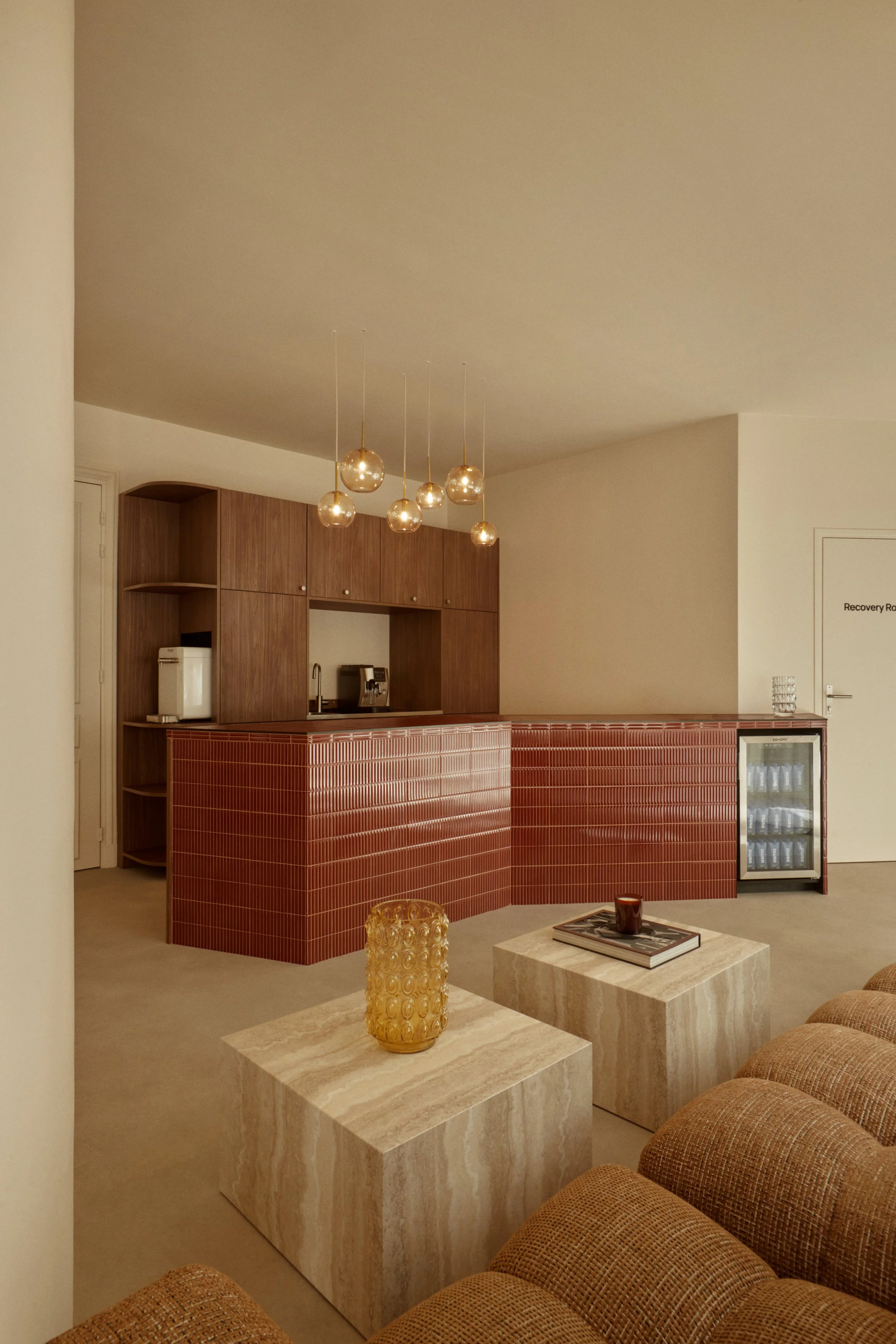Comptoir d’accueil en carreaux brun-rouge, mobilier bois et salon lounge pour un studio de sport et wellness à Paris conçu par Local Club.