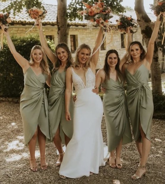 Bride in a white wedding dress standing with four bridesmaids in green dresses, holding bouquets, smiling outdoors.
