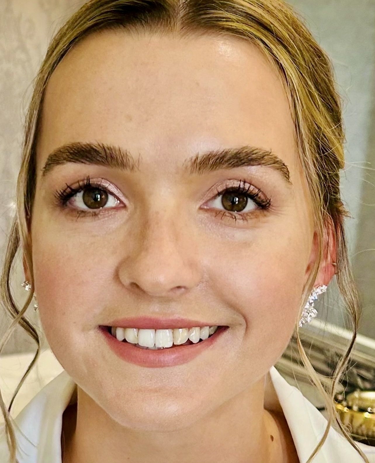 Close-up of a woman with blonde hair, brown eyes, fair skin, and jewelry smiling at the camera.