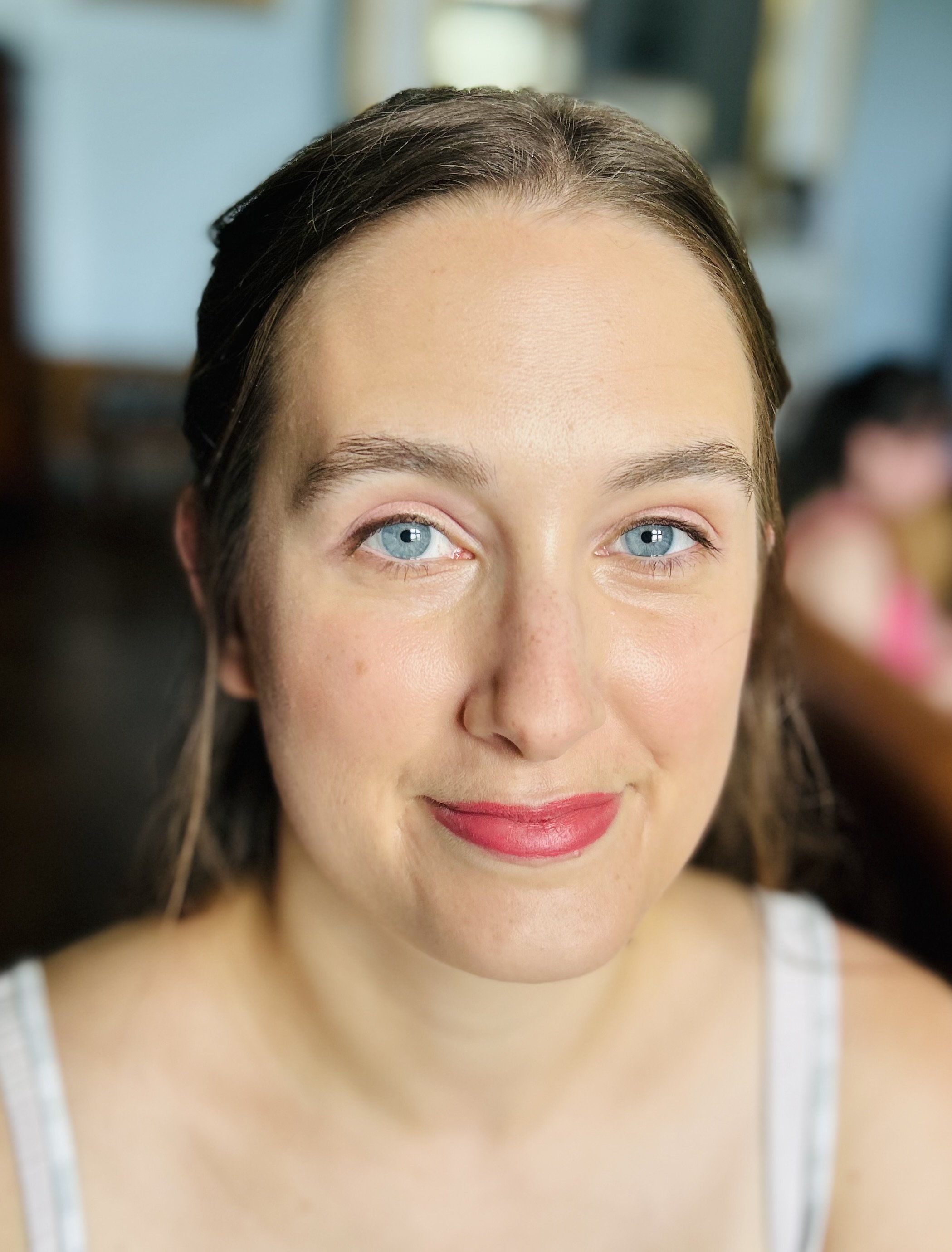 Close-up of a woman with blue eyes and brown hair, smiling gently, with blurred background.
