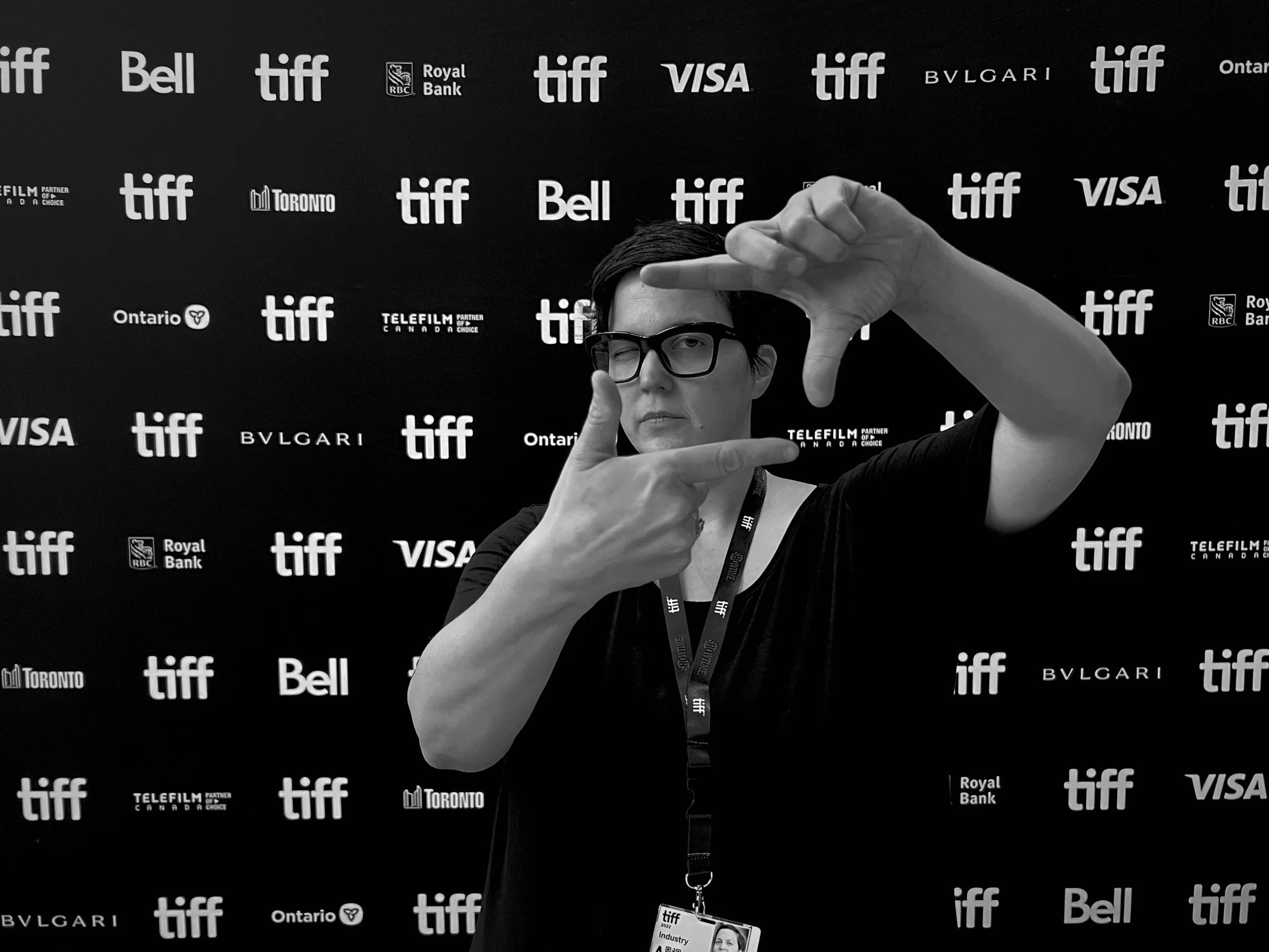 Person with short dark hair and glasses making a framing gesture with hands in front of TIFF backdrop.