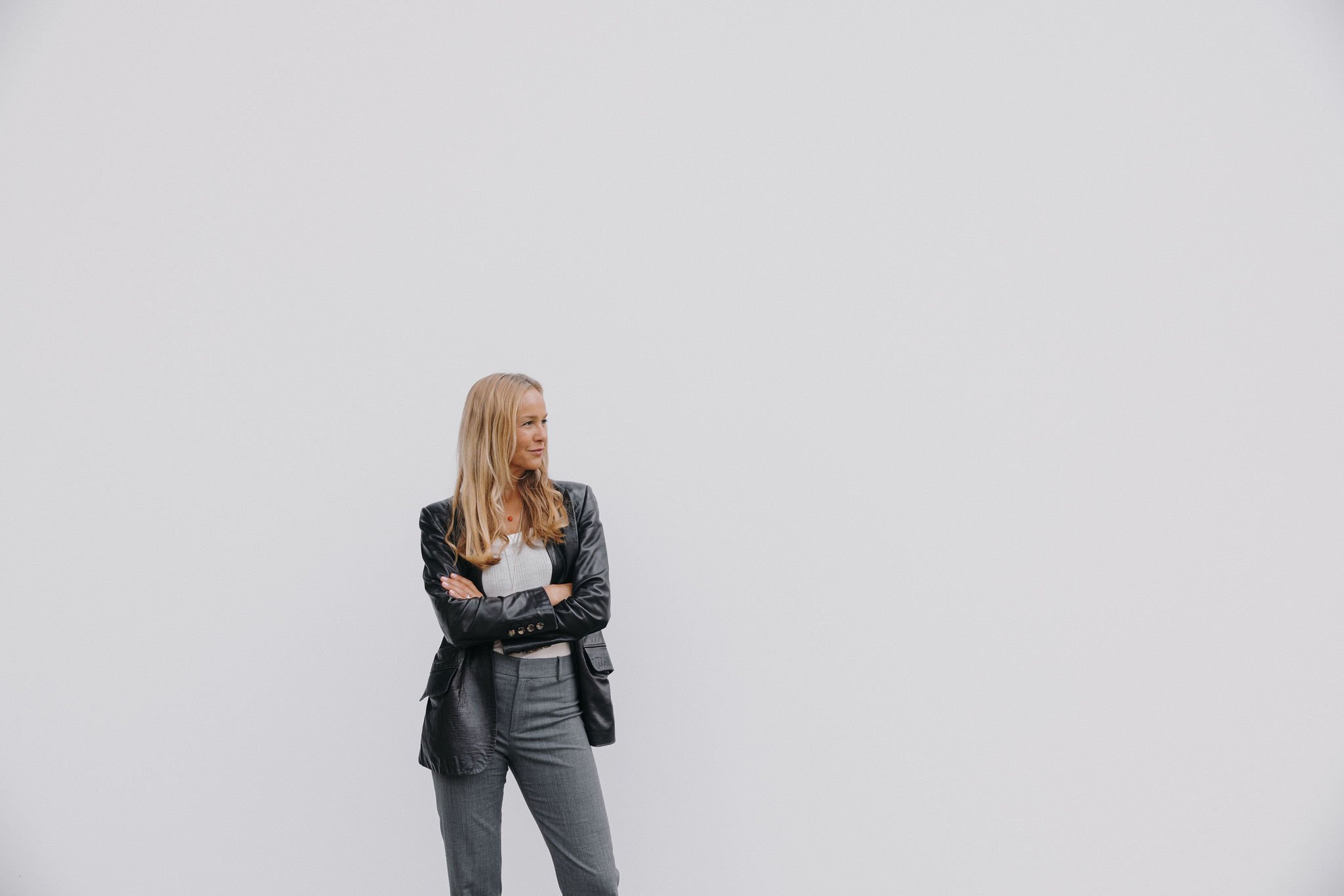A woman standing with arms crossed in front of a plain white background.