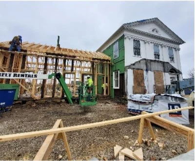 Construction site with workers and wooden framework next to an older building