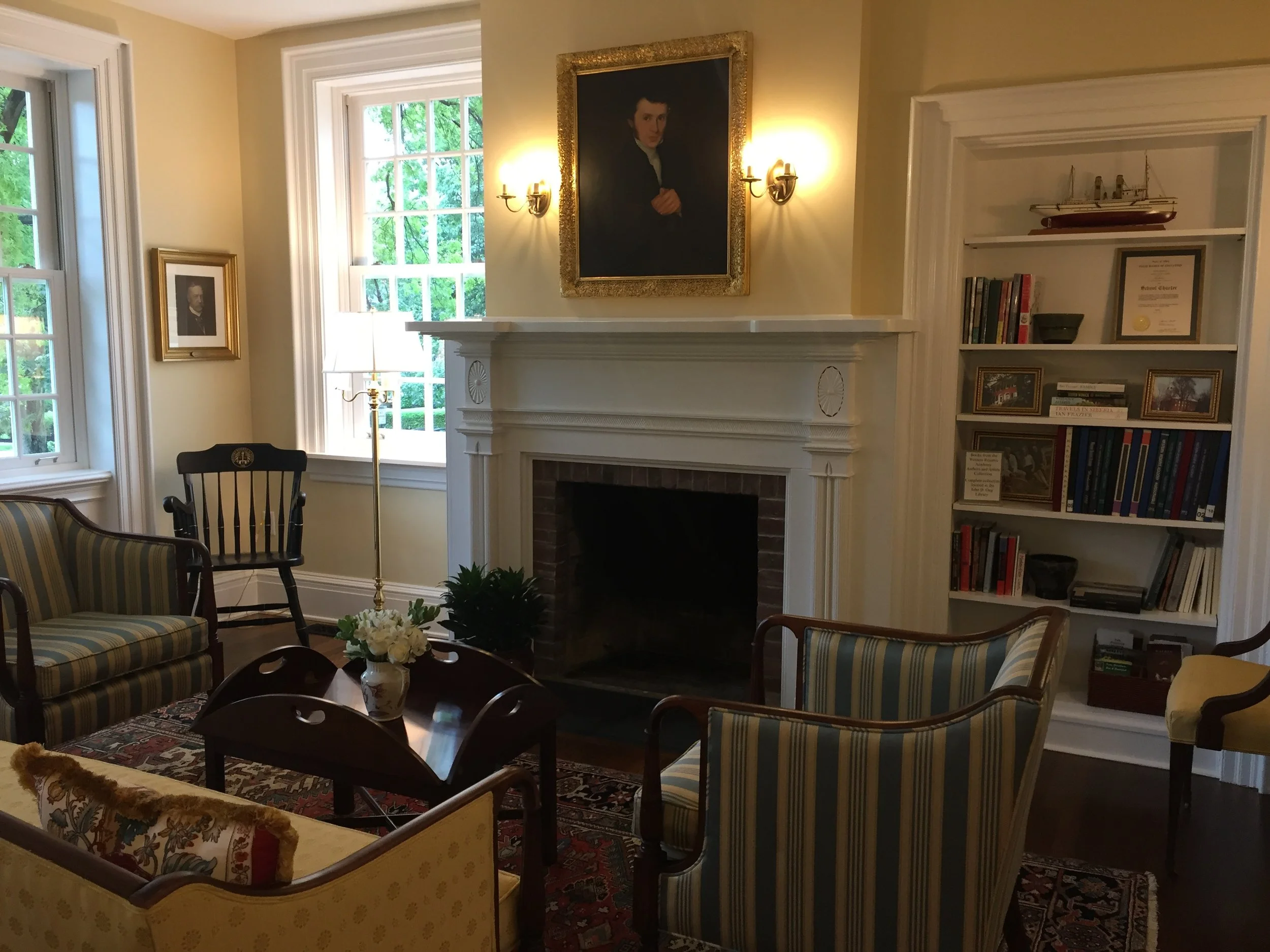 Elegant living room with classic striped seating, fireplace, portrait art, bookshelf, model ship, and decorative rug.