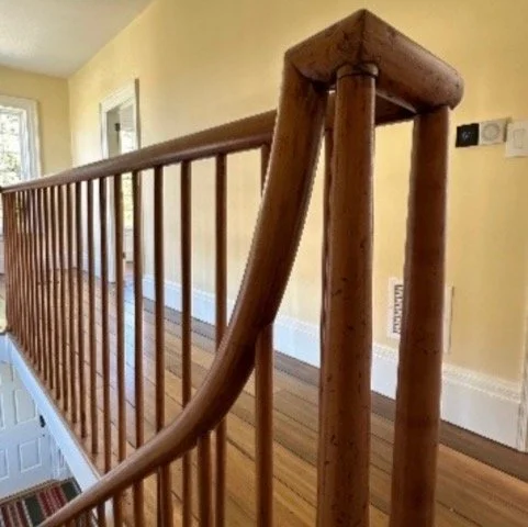 Wooden staircase railing with spindles in a well-lit hallway.
