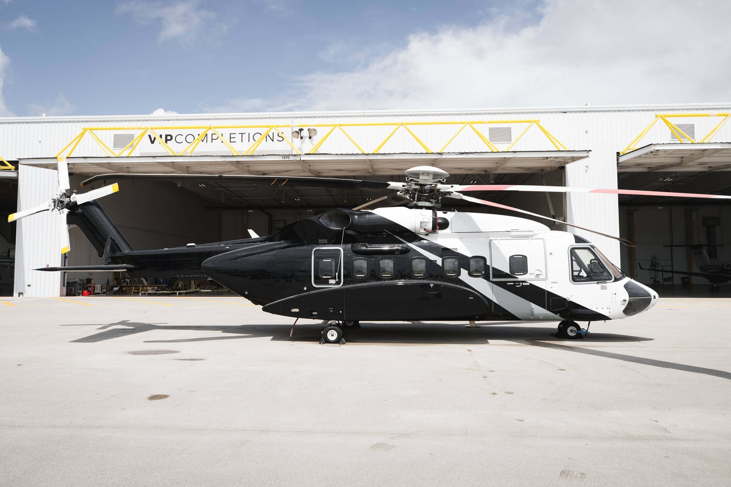 A black and white helicopter parked outside a hangar labeled VIP Completions.