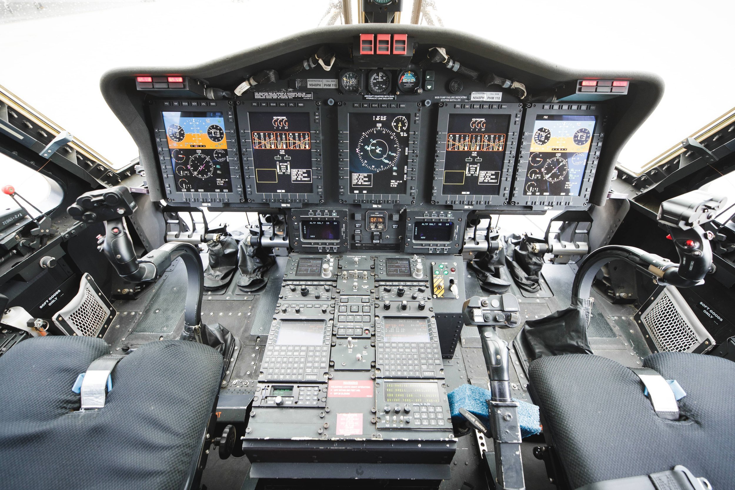 Inside view of an aircraft cockpit with multiple digital and analog gauges, control panels, and two pilot seats.