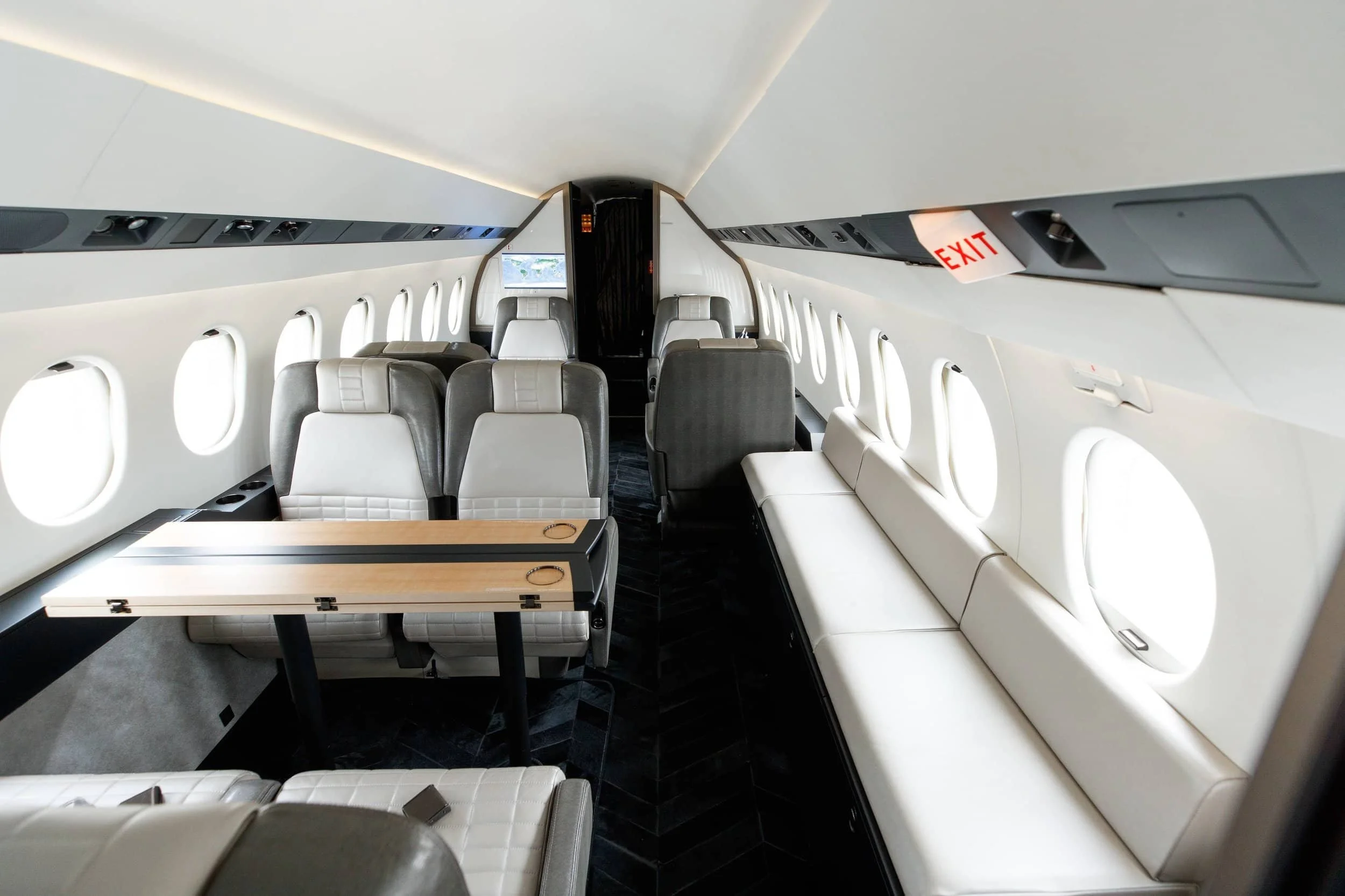 Inside the cabin of a private jet with cream-colored leather seats, a small wooden table, and large windows on both sides.