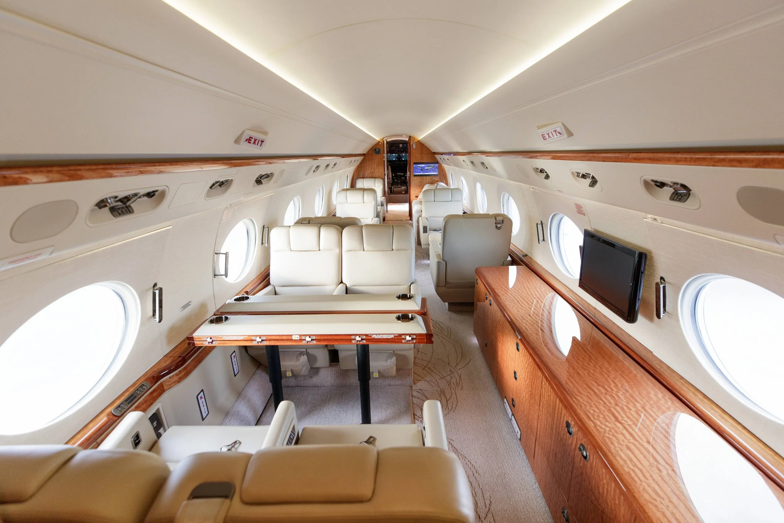 Interior of a private jet with beige leather seats, wooden cabinetry, and windows on the sides.