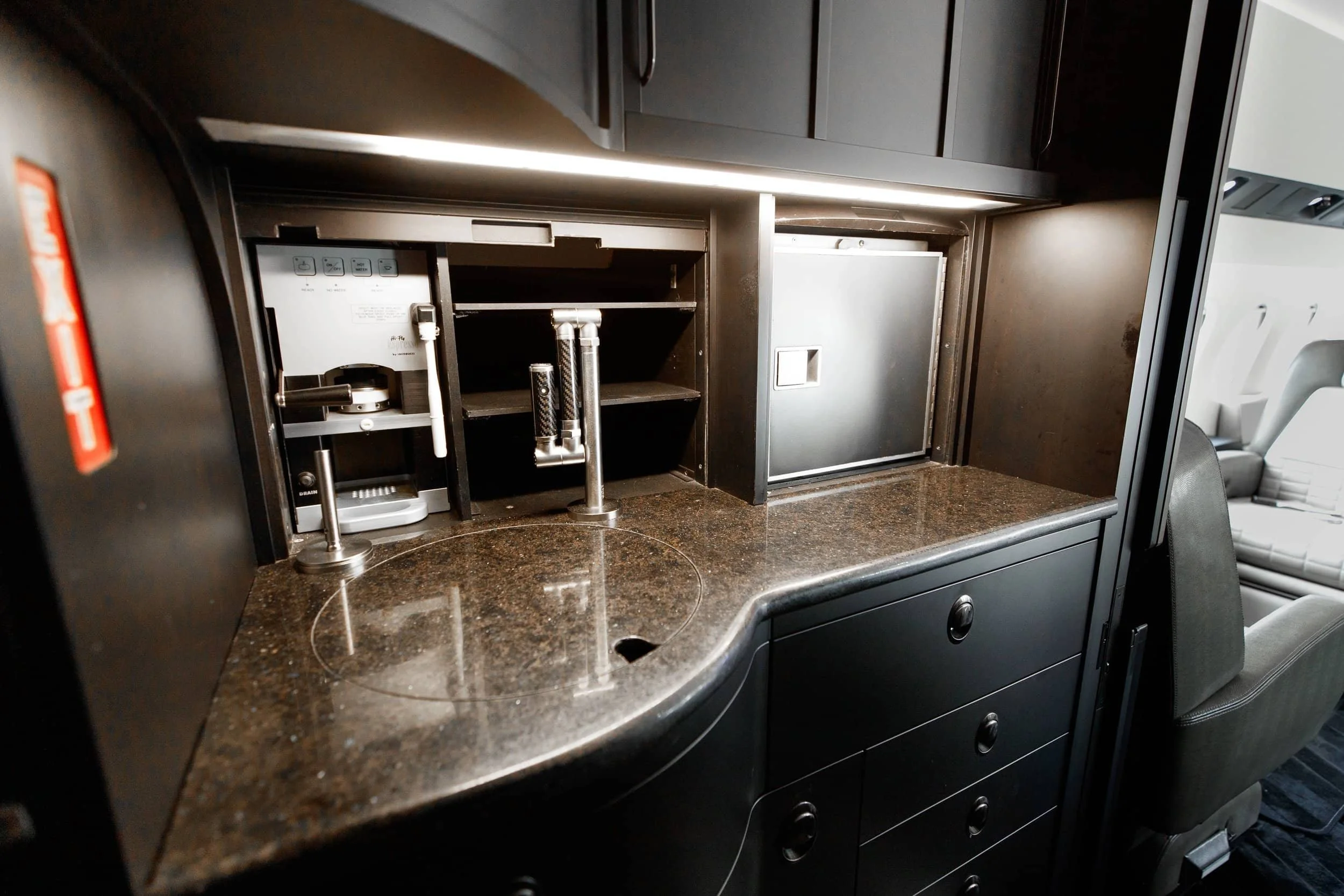 Interior of an aircraft with a coffee station including a coffee maker and storage compartments.