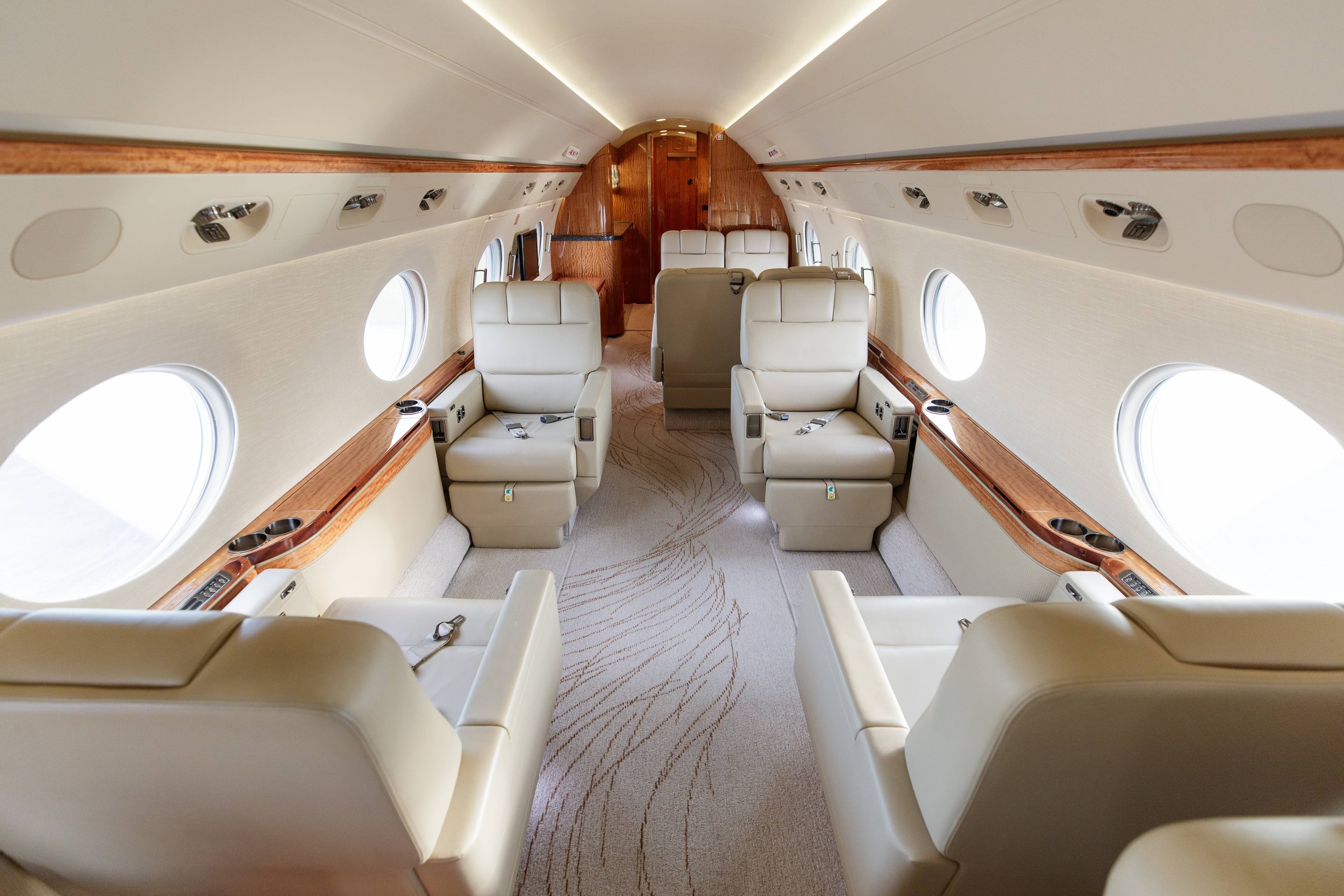 Interior of a private jet with beige leather seats, wooden accents, and multiple oval windows.