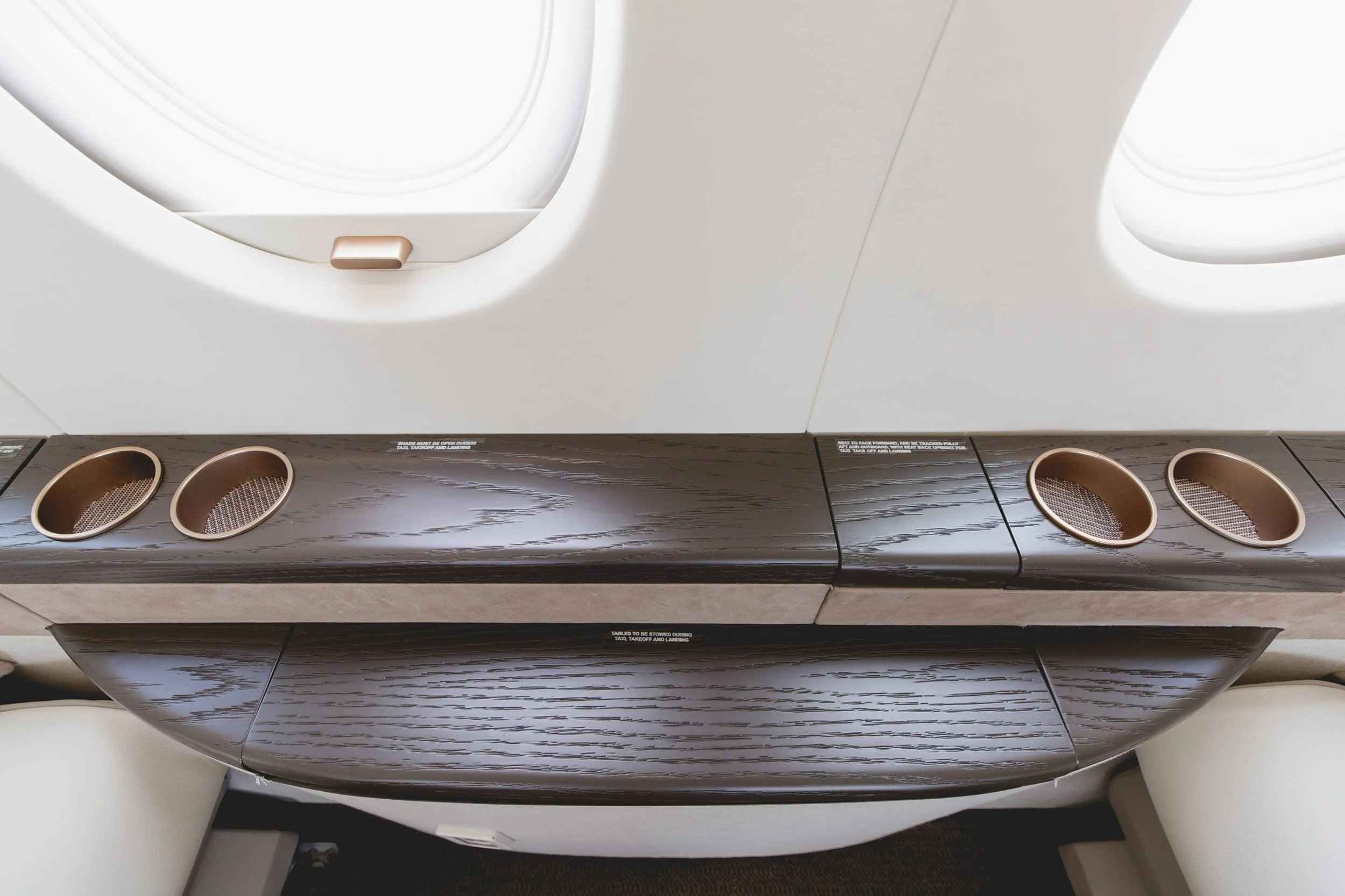 View of airplane window with a dark wood tray table and cup holders underneath the window.
